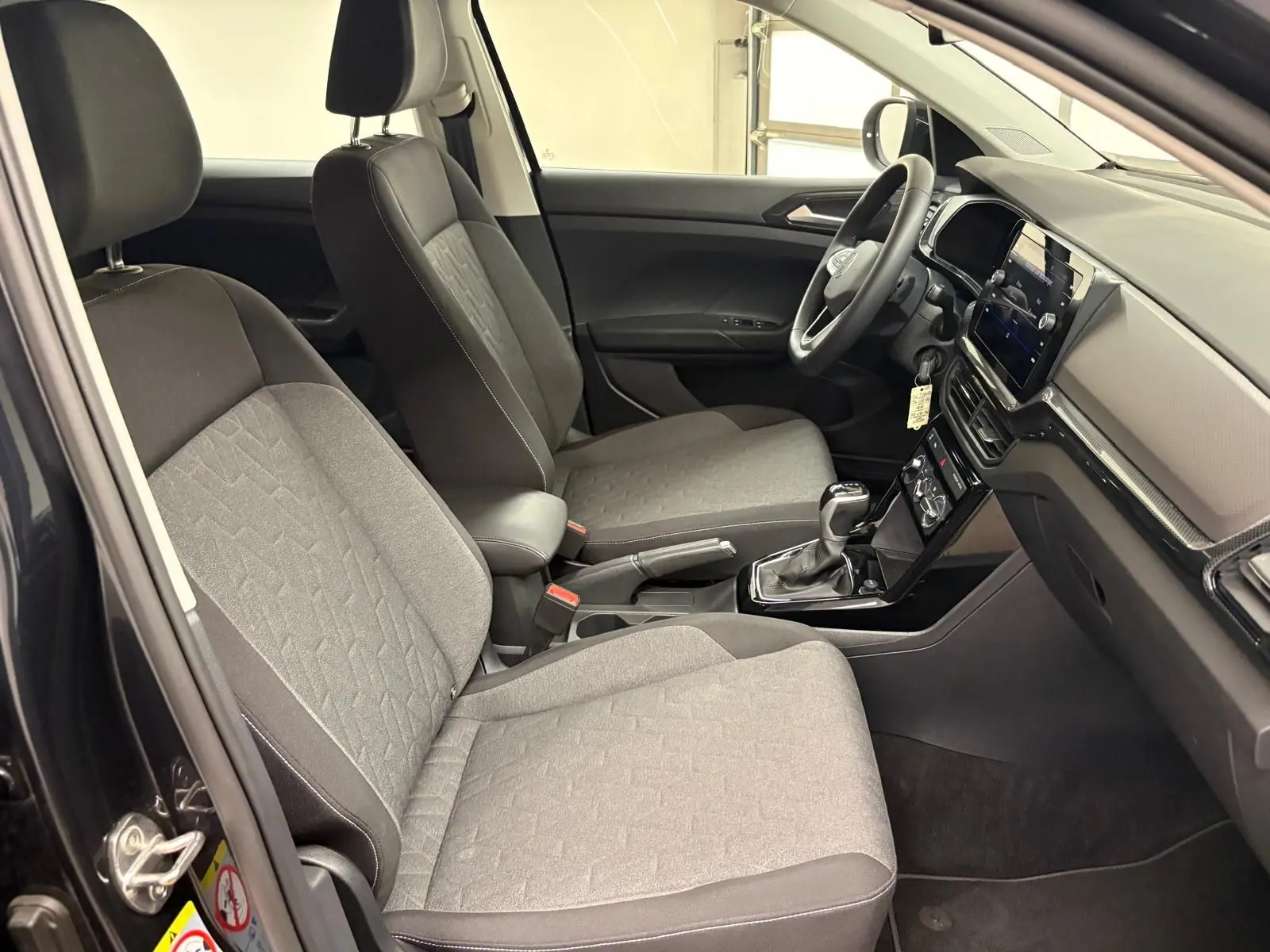 Vue intérieure côté conducteur du Volkswagen T-Cross 2024 avec sièges gris et tableau de bord moderne.