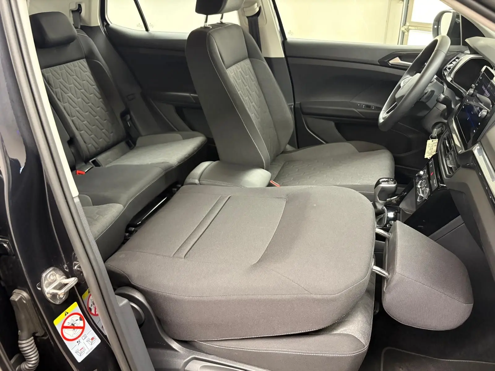 Intérieur du Volkswagen T-Cross noir intense 2024, vue côté gauche avec sièges avant rabattus et tableau de bord visible.