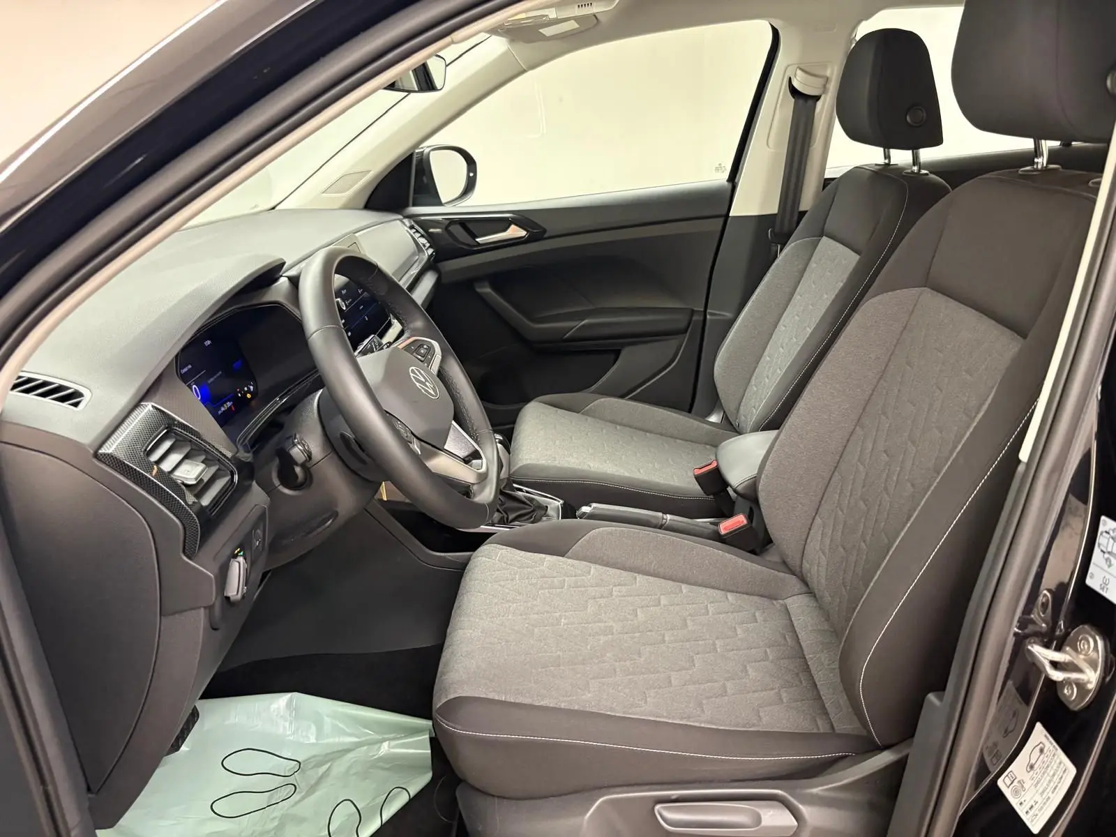 Vue intérieure côté conducteur du Volkswagen T-Cross 2024 noir intense, sièges tissu gris et tableau de bord moderne.