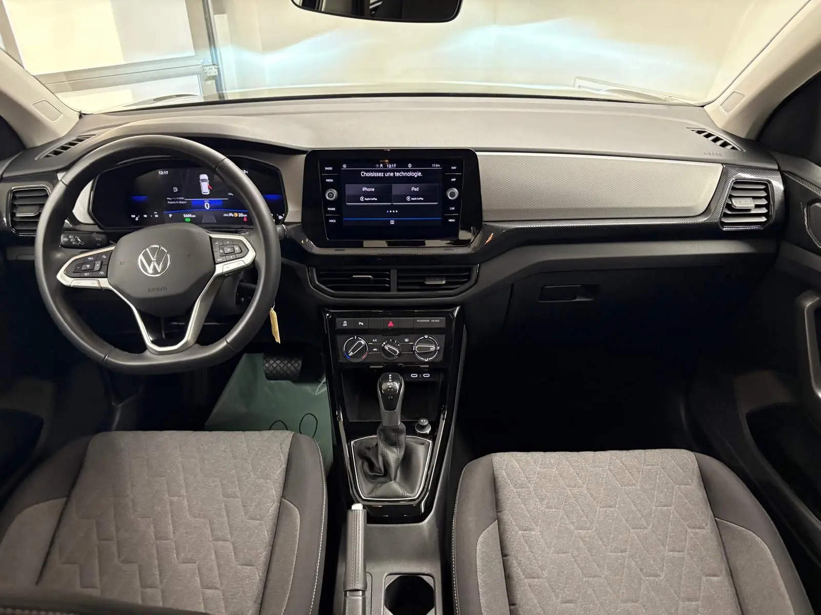 Vue intérieure frontale du tableau de bord et volant du Volkswagen T-Cross 2024 avec écran tactile et sièges gris.