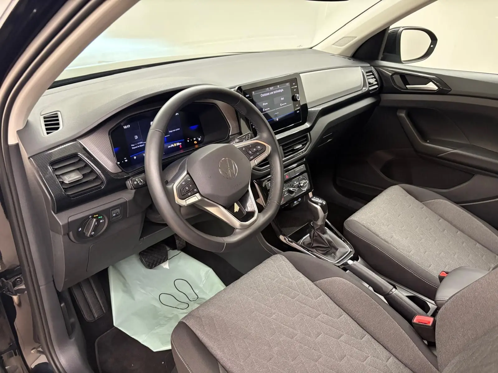 Intérieur du Volkswagen T-Cross 2024 vu côté conducteur, tableau de bord moderne avec écran tactile et sièges gris.