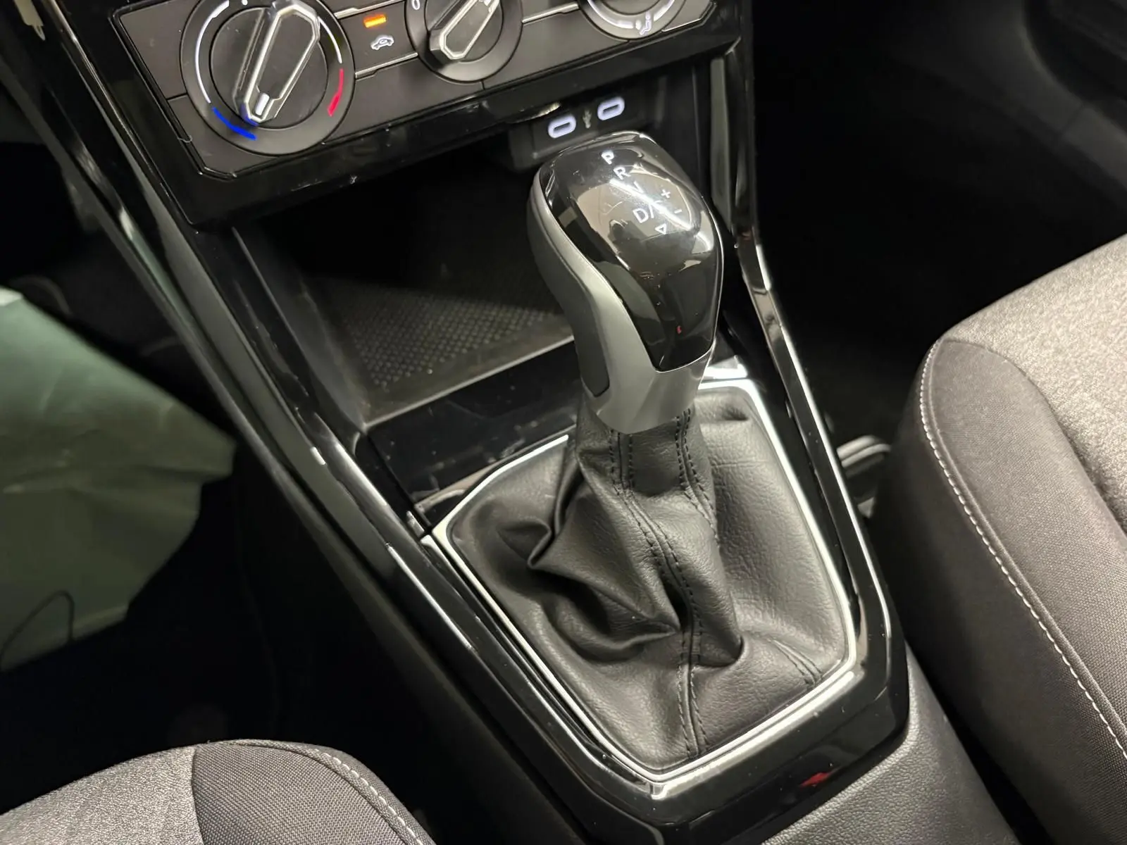 Le levier de vitesses automatique noir brillant du Volkswagen T-Cross 2024, avec console et sièges gris.