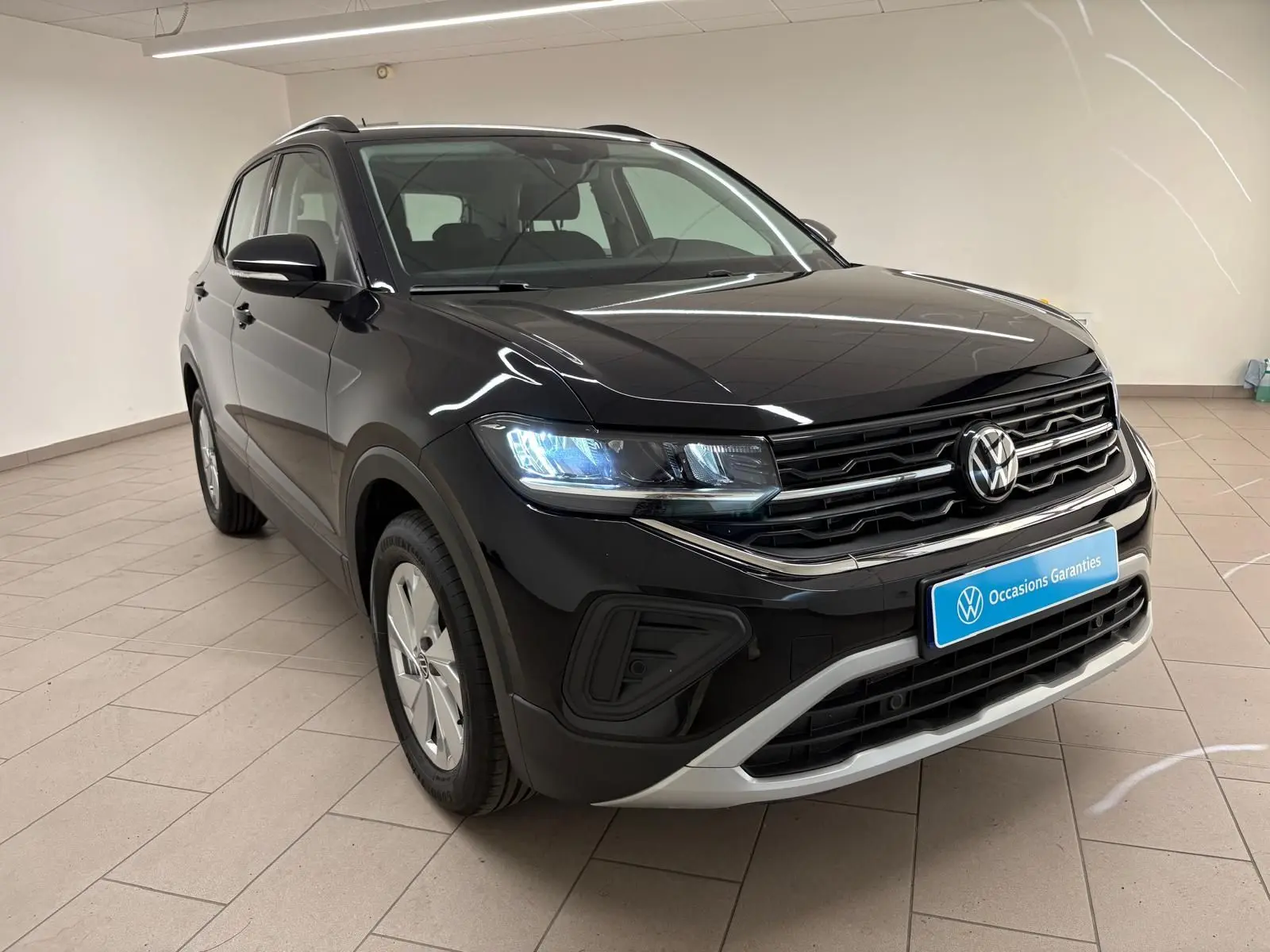 Volkswagen T-Cross noir intense en 3/4 avant droit, avec calandre chromée et phares LED allumés dans un showroom.