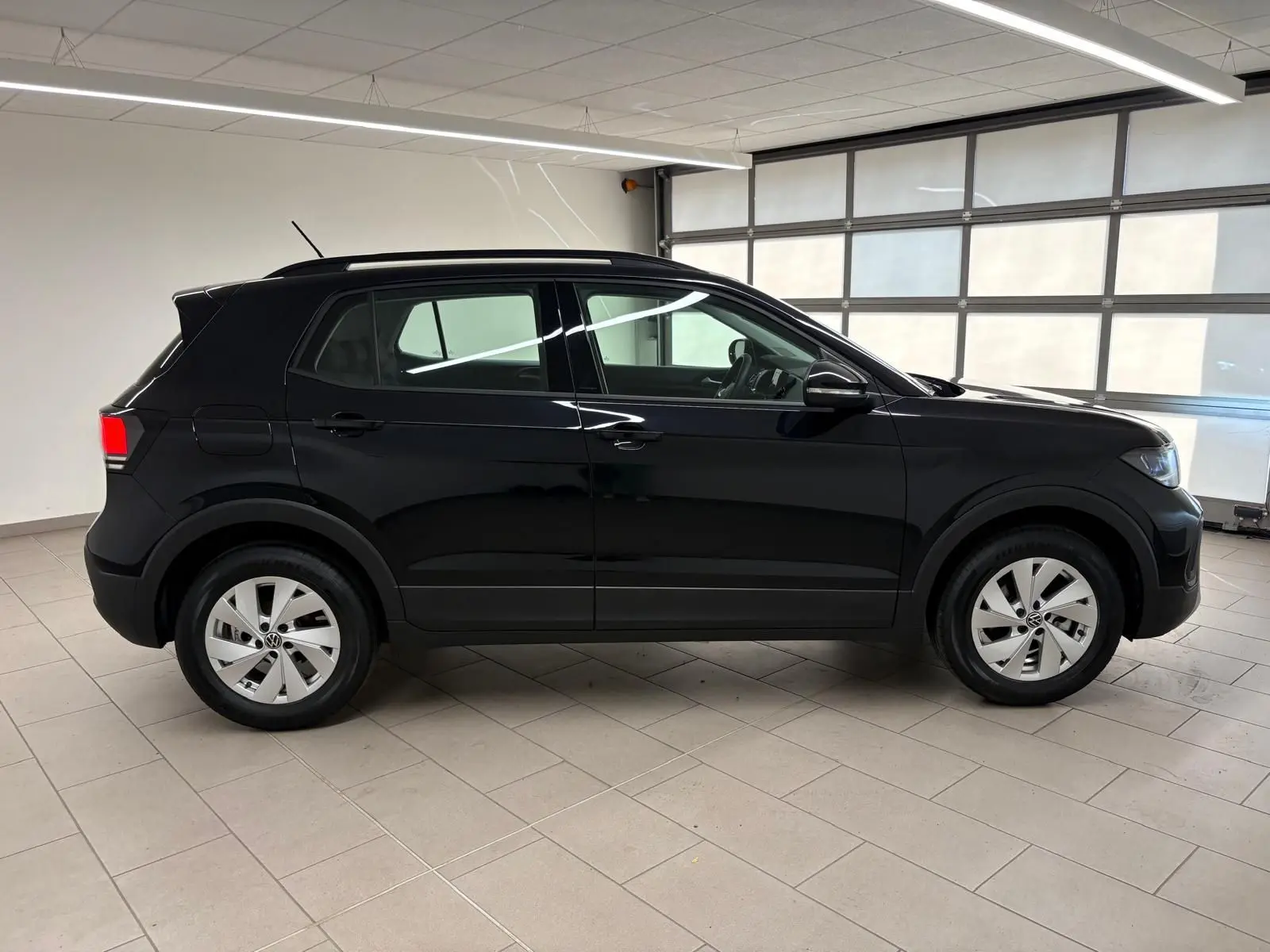 Profil côté droit du Volkswagen T-Cross 2024 noir intense avec jantes alliage dans un garage lumineux.
