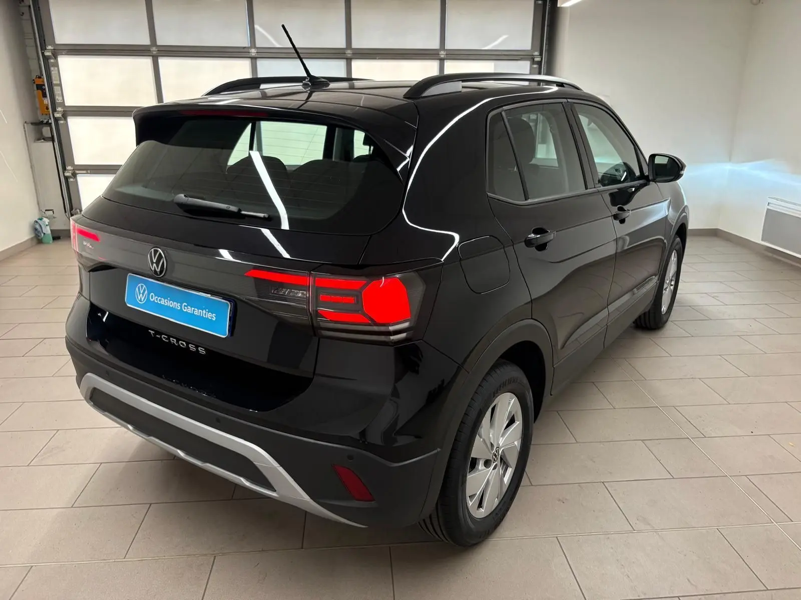 Volkswagen T-Cross noir intense vu en 3/4 arrière droit dans un garage avec feux arrière allumés.