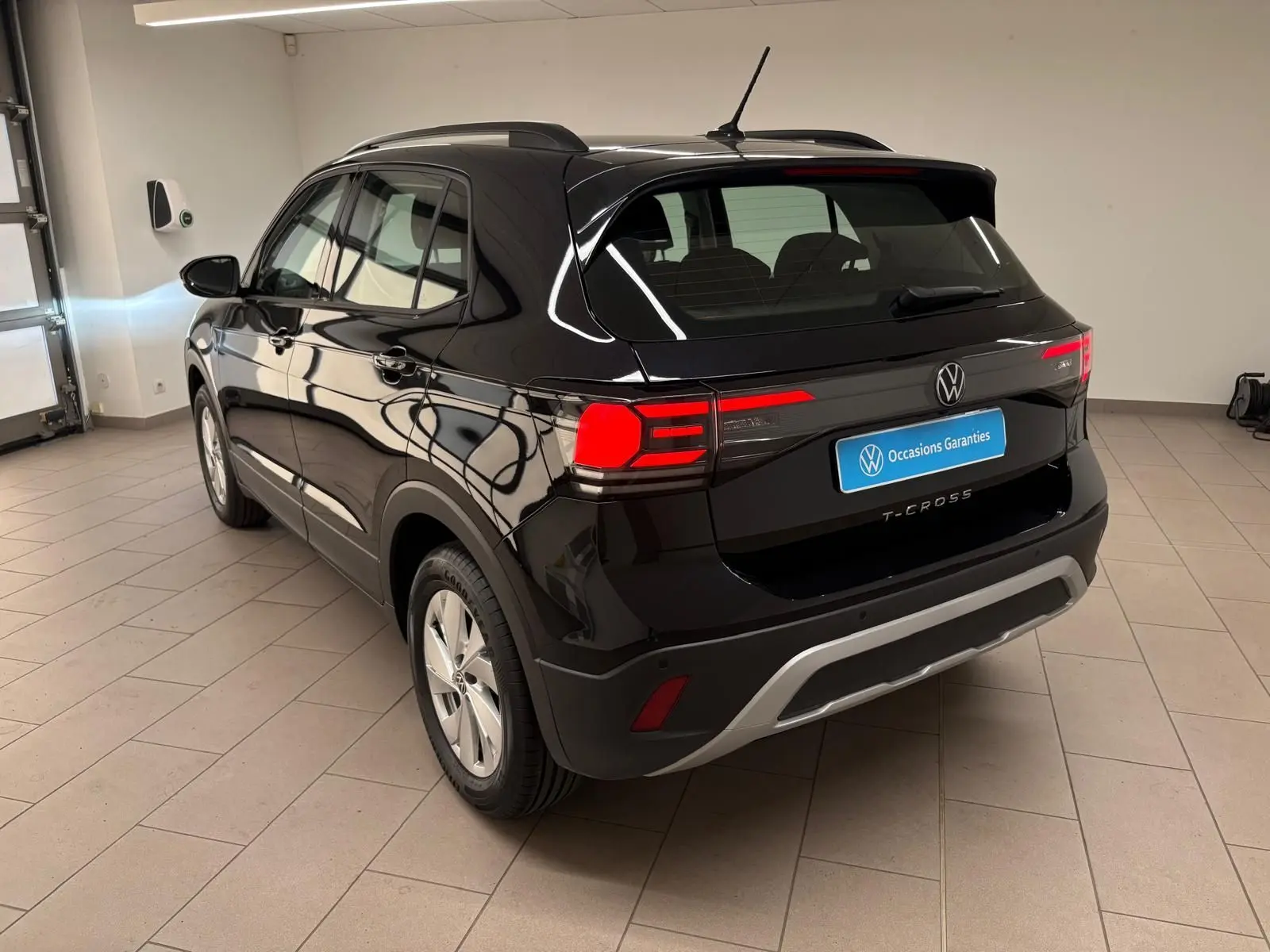 Volkswagen T-Cross noir intense vue 3/4 arrière droit en intérieur, avec feux arrière allumés et jantes argentées.