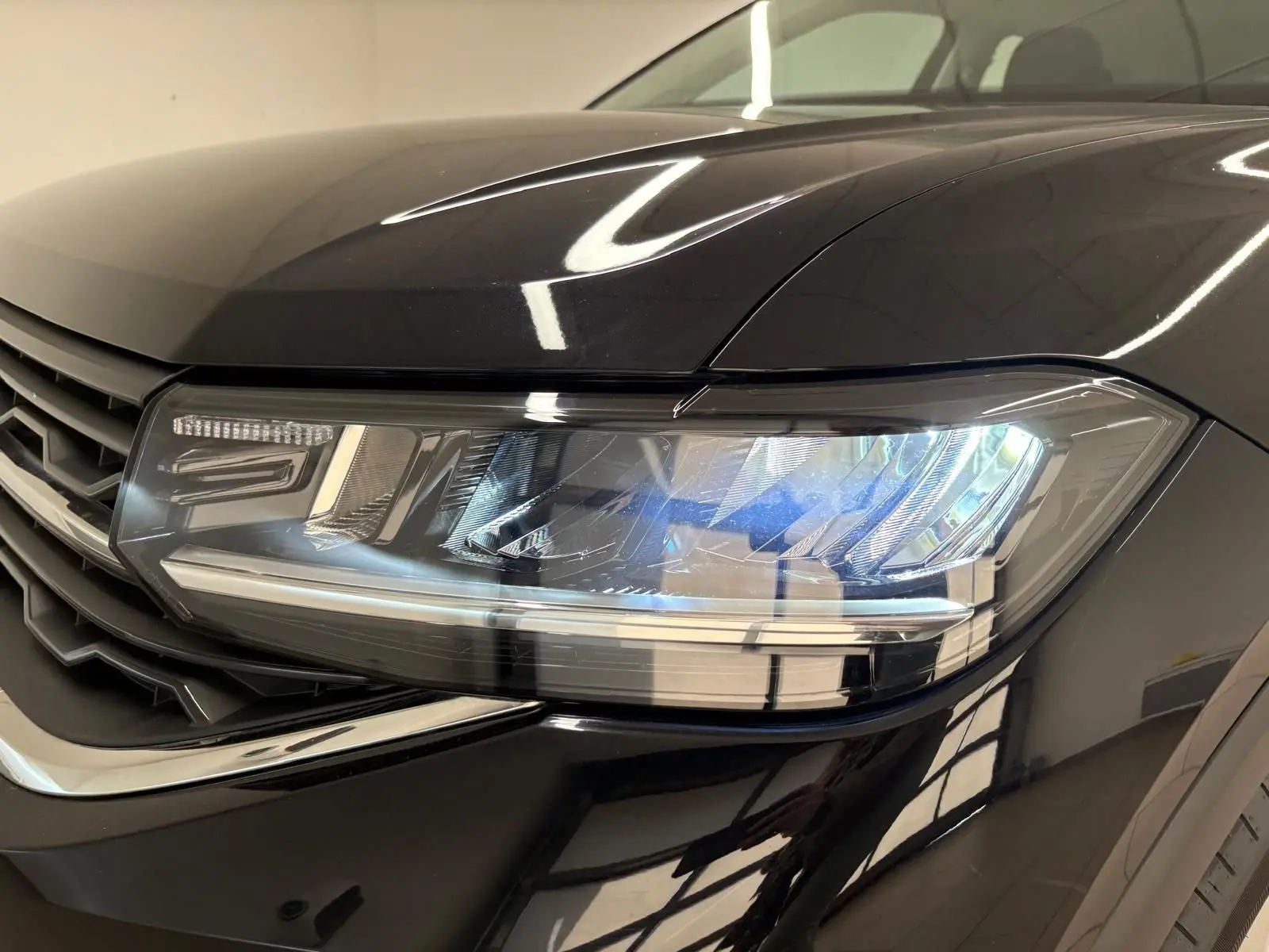 Gros plan sur le phare avant droit du Volkswagen T-Cross 2024 noir intense avec peinture métallisée brillante.