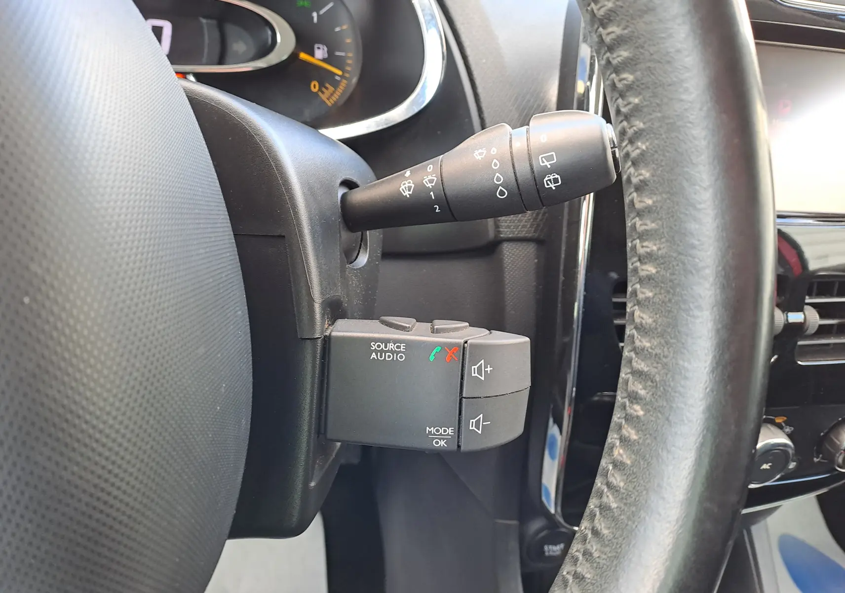 Gros plan sur la commande audio au volant côté gauche d’une Renault Clio IV rouge, avec levier d’essuie-glace visible.