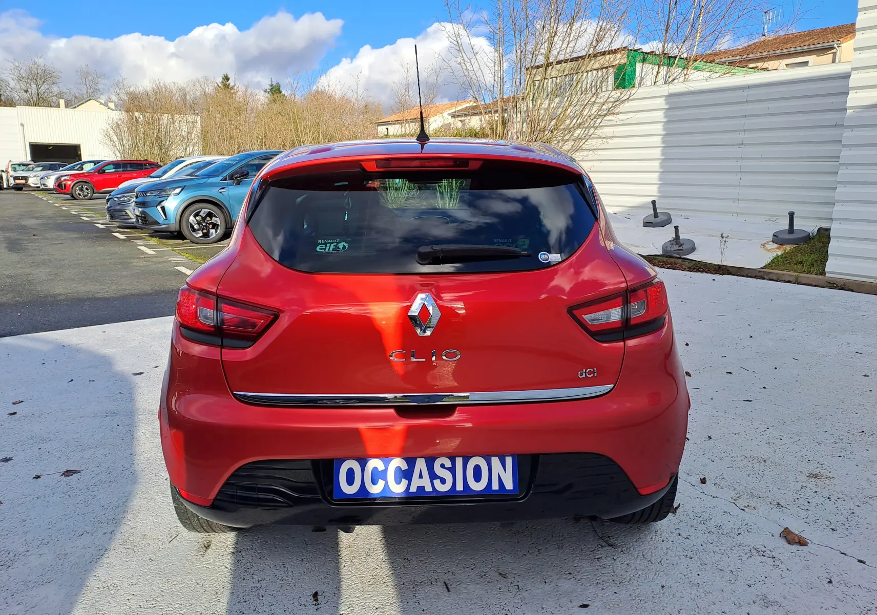 Vue arrière d'une Renault Clio IV rouge 1.5 dCi avec plaque "OCCASION" sur un parking extérieur.