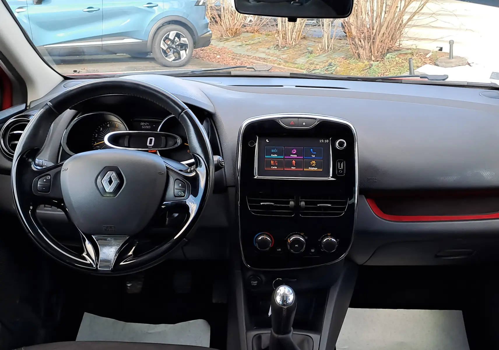 Vue intérieure frontale du tableau de bord noir et volant Renault d'une Clio IV rouge avec écran tactile et levier de vitesse manuel.