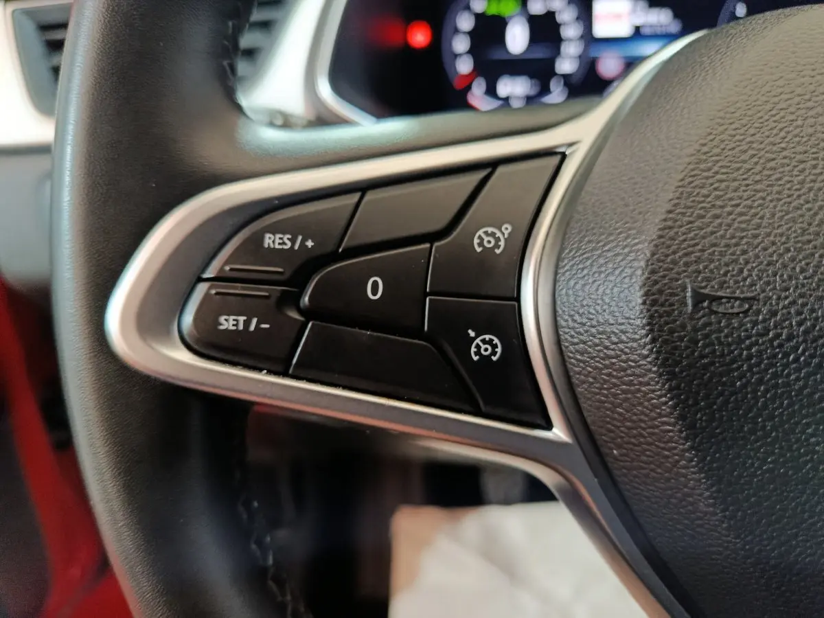 Gros plan sur les commandes de régulateur de vitesse au volant du Renault Captur rouge, intérieur visible en arrière-plan.