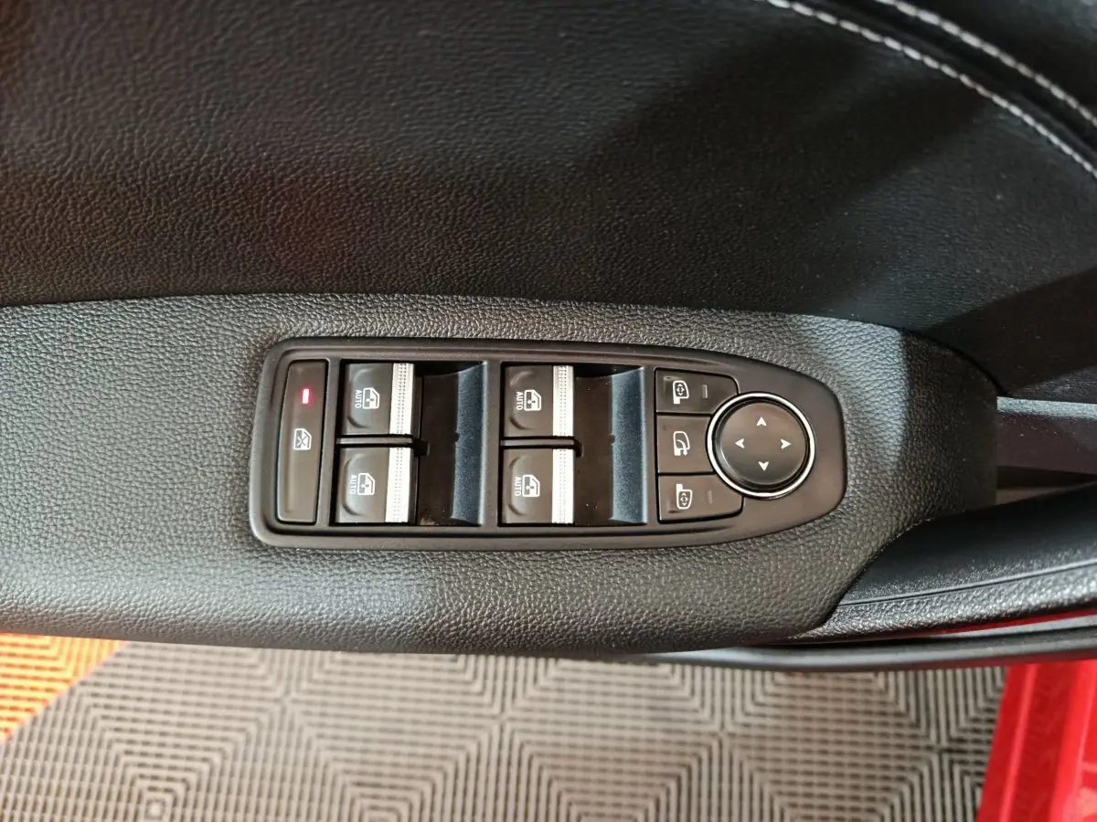 Commande des vitres et rétroviseurs sur la porte côté conducteur d’un Renault Captur rouge 2024, vue en plongée.