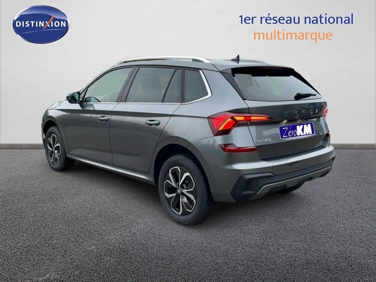 Vue 3/4 arrière droite du Skoda Kamiq gris graphite métal avec feux arrière allumés sur fond neutre.