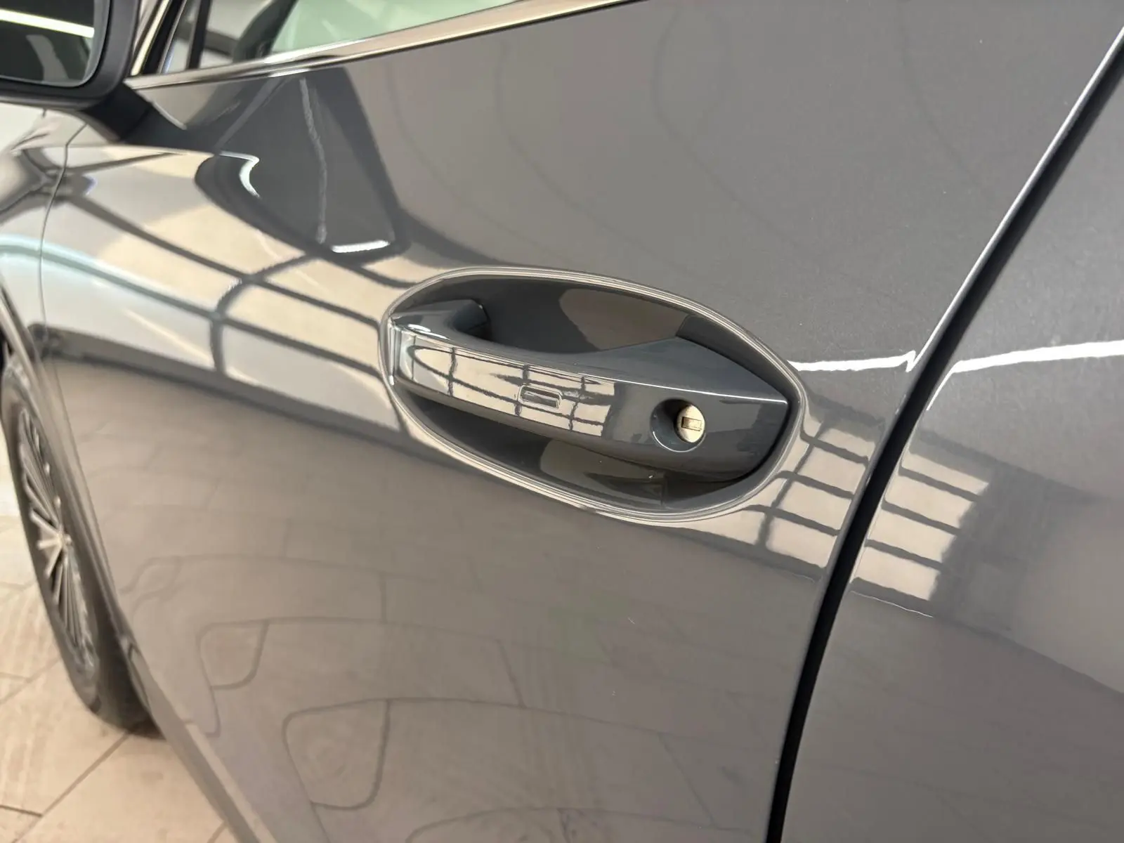 Poignée de porte côté gauche en gros plan sur Volkswagen Tiguan 2025 gris dauphin métallisé, reflet lumineux sur la carrosserie.