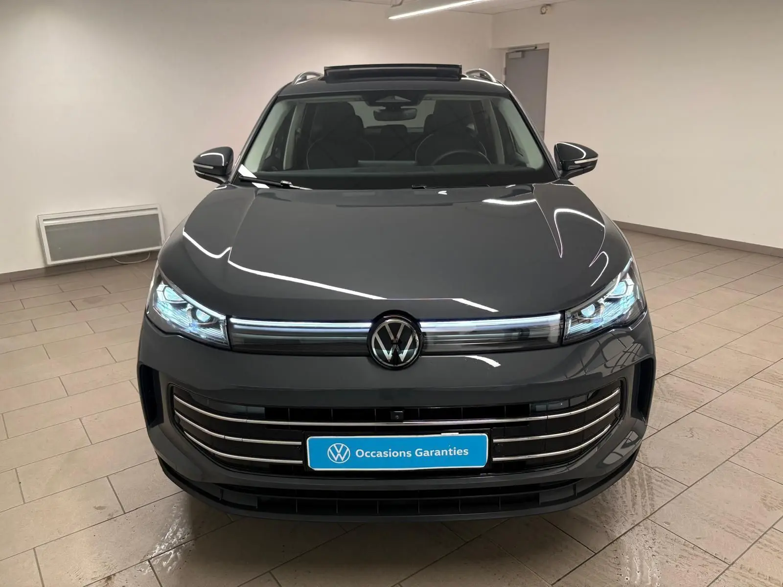 Vue de face du Volkswagen Tiguan 2.0 TDI 150 DSG7 Elegance en gris dauphin métallisé, avec phares allumés dans un intérieur neutre.