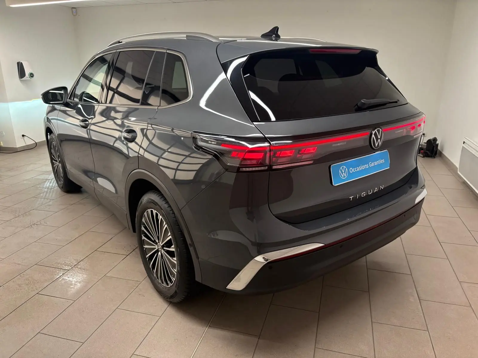 Vue 3/4 arrière droite d'un Volkswagen Tiguan gris dauphin métallisé, avec feux arrière allumés et jantes stylisées.