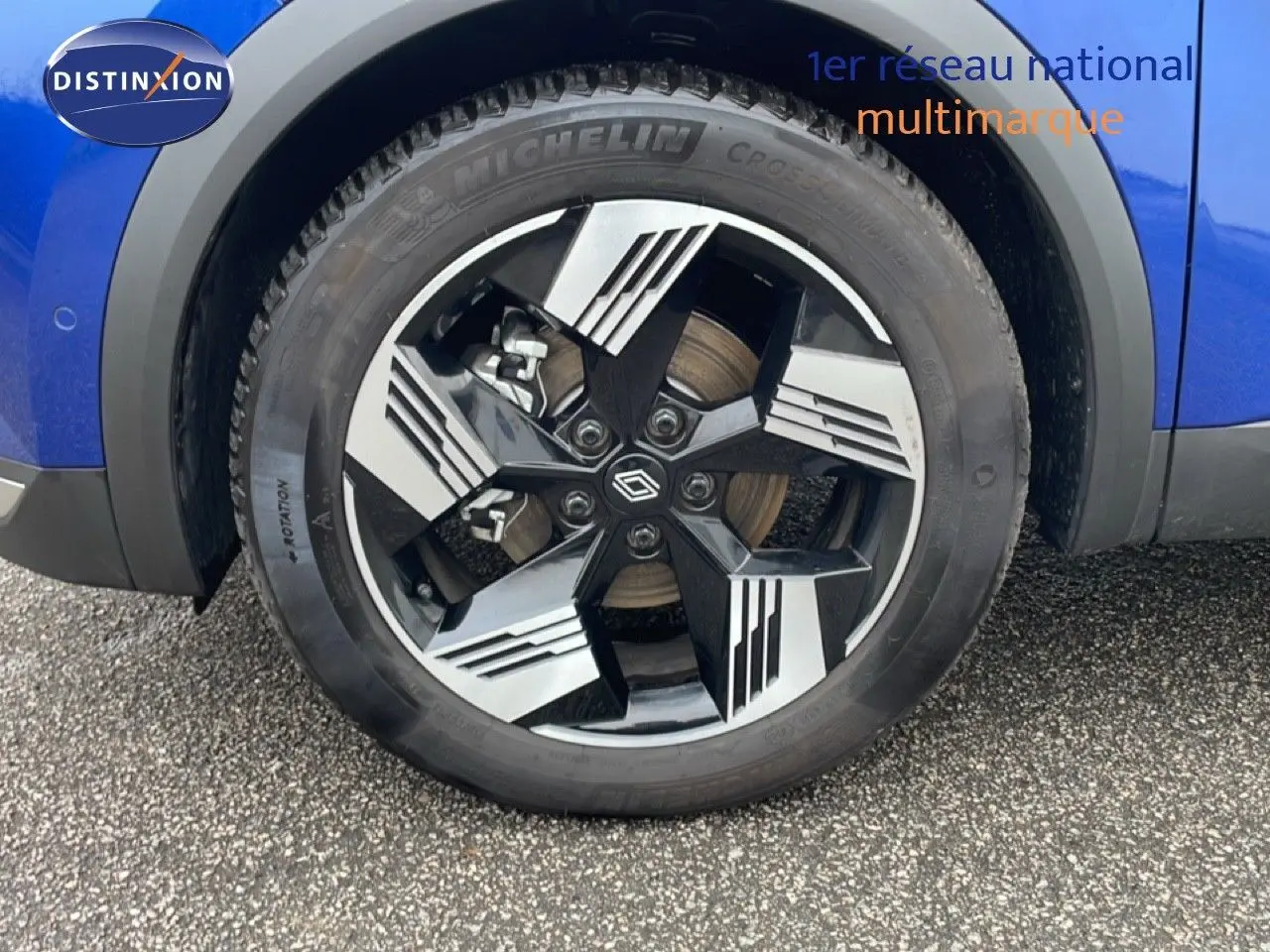 Gros plan sur la roue avant droite d'une Renault Symbioz bleu iron metal avec jante noire et argentée au design moderne.