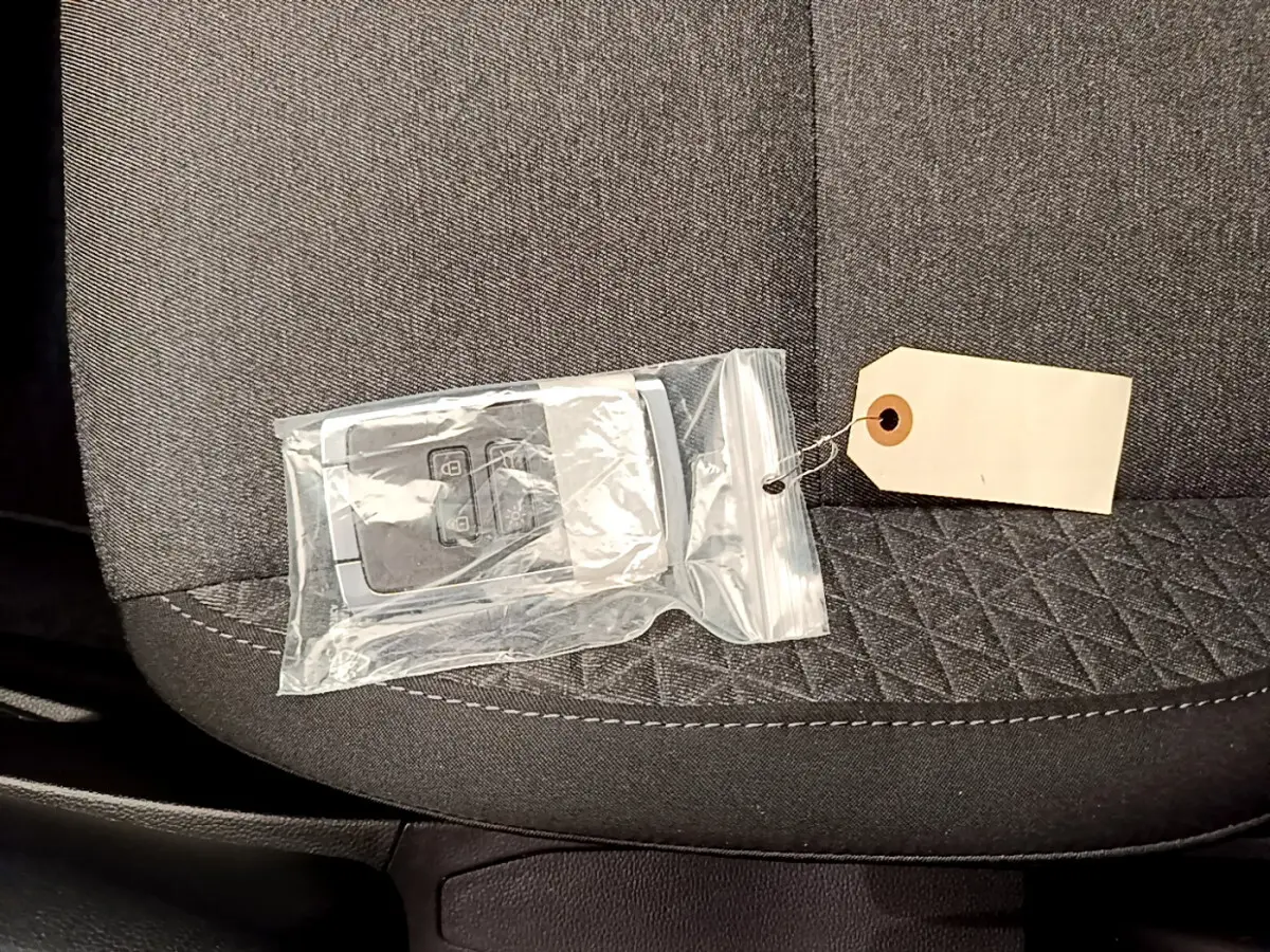 Gros plan sur une clé de voiture Renault Clio Business TCe 100 2020 dans un sachet plastique, posée sur un siège tissu gris.