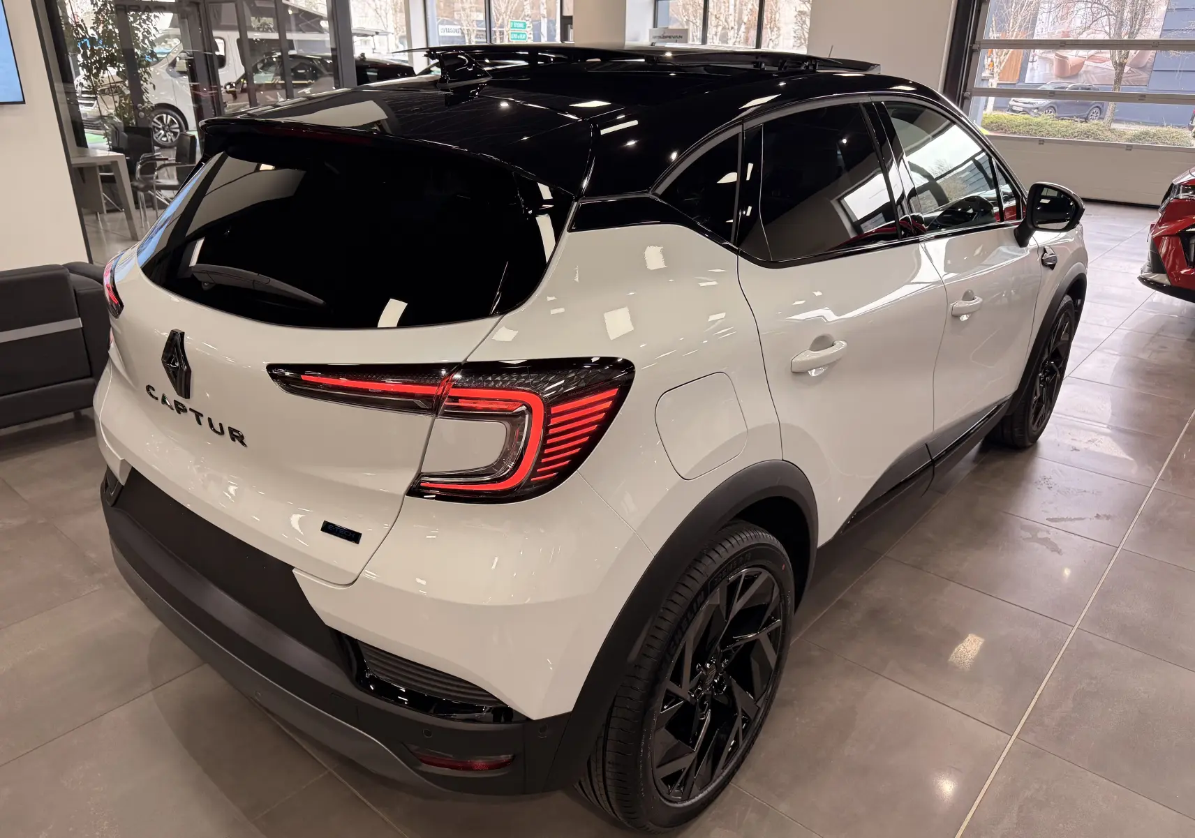 Vue 3/4 arrière droite du Renault Captur blanc nacré avec toit noir et jantes noires en showroom.