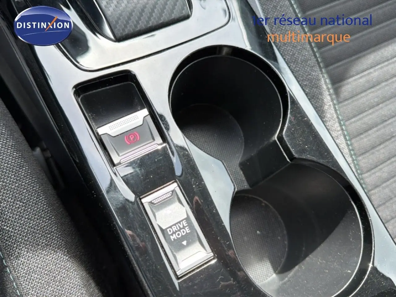Gros plan sur la console centrale noire perle métal du Peugeot 2008, avec boutons frein à main électronique et mode de conduite.