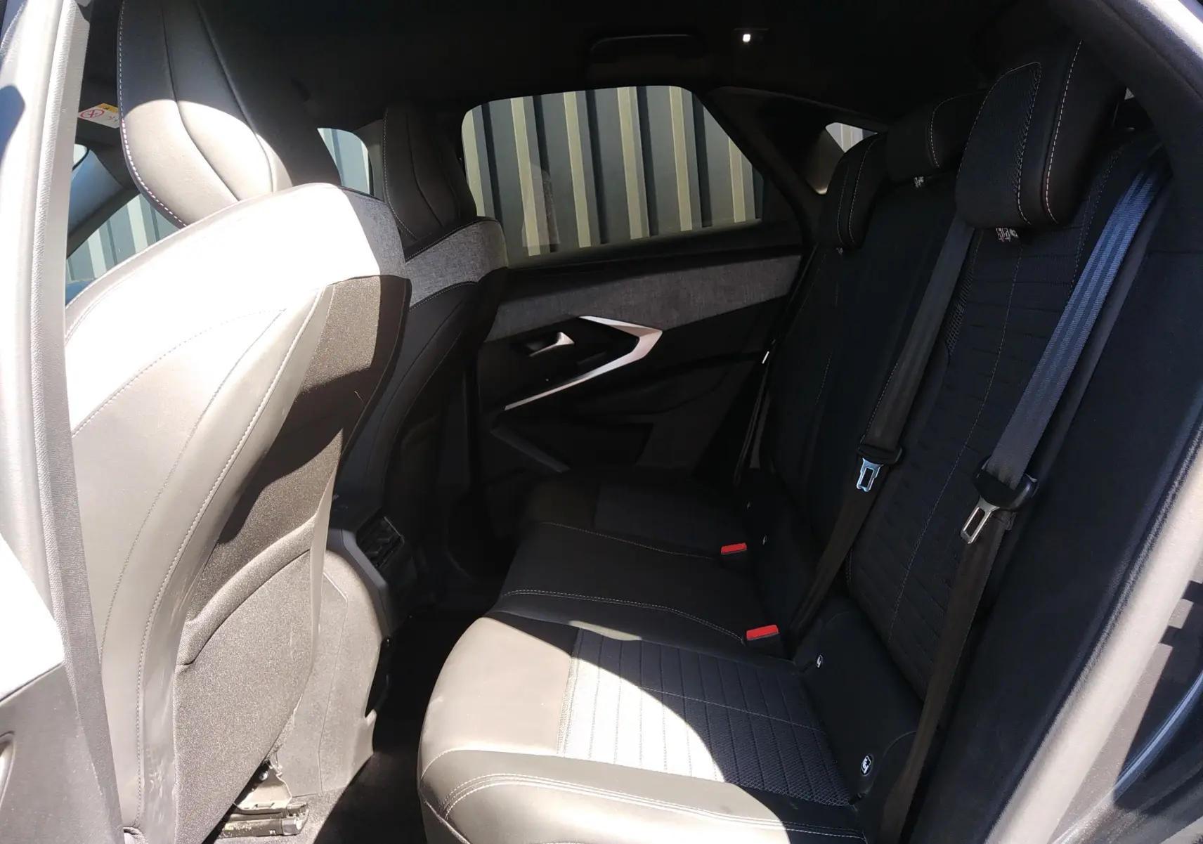 Vue intérieure arrière côté gauche du Peugeot 3008 Hybrid 136 Allure 2024 avec sièges en tissu noir et gris.