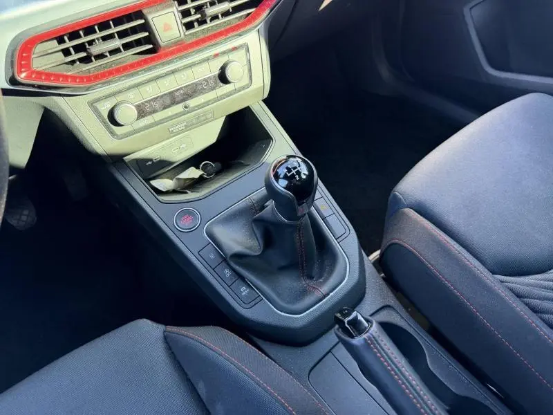 Vue rapprochée de la console centrale de la SEAT Ibiza 2025, boîte manuelle avec coutures rouges et détails noirs.