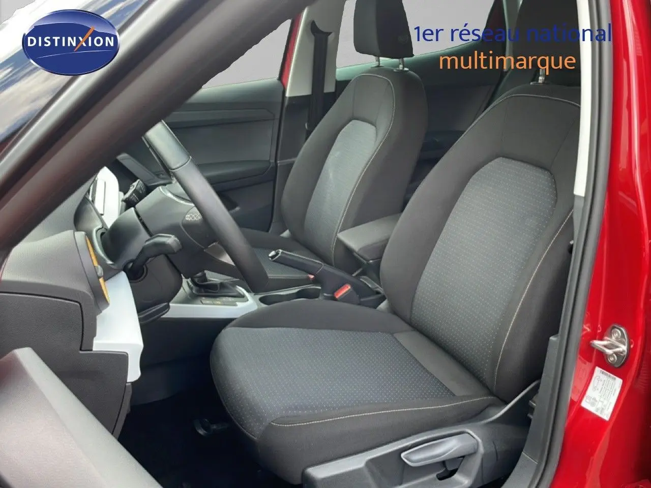 Vue intérieure côté conducteur du SEAT Arona rouge désir métal, montrant les sièges en tissu noir et le volant multifonction.