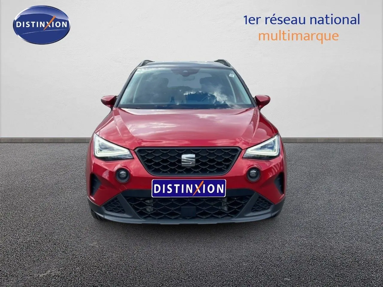 Vue frontale d'un SEAT Arona rouge désir métal avec toit noir, mettant en valeur ses phares LED et sa calandre noire.