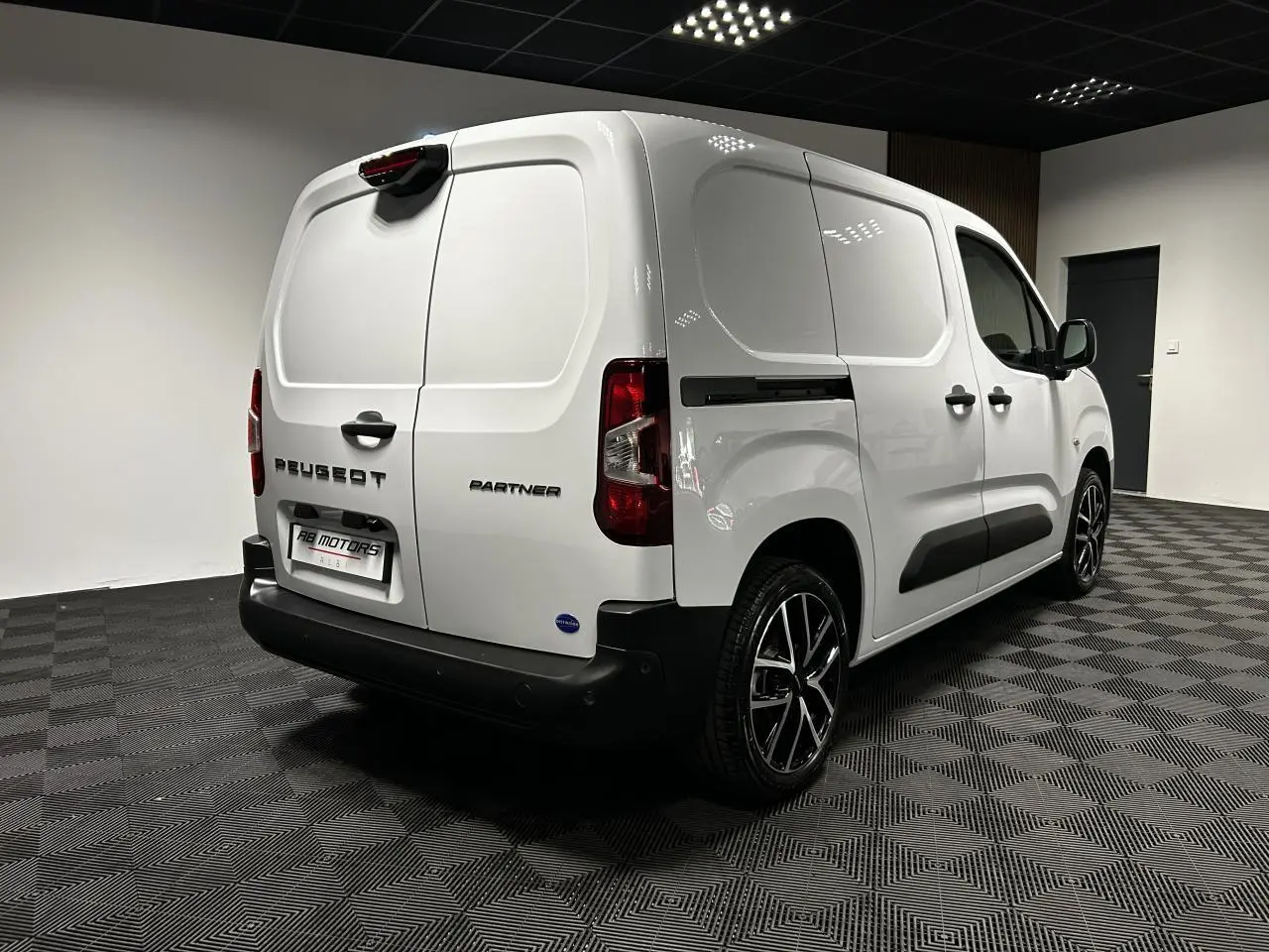 Vue 3/4 arrière droite du Peugeot Partner blanc Banquise avec jantes alu 17 pouces dans un showroom.