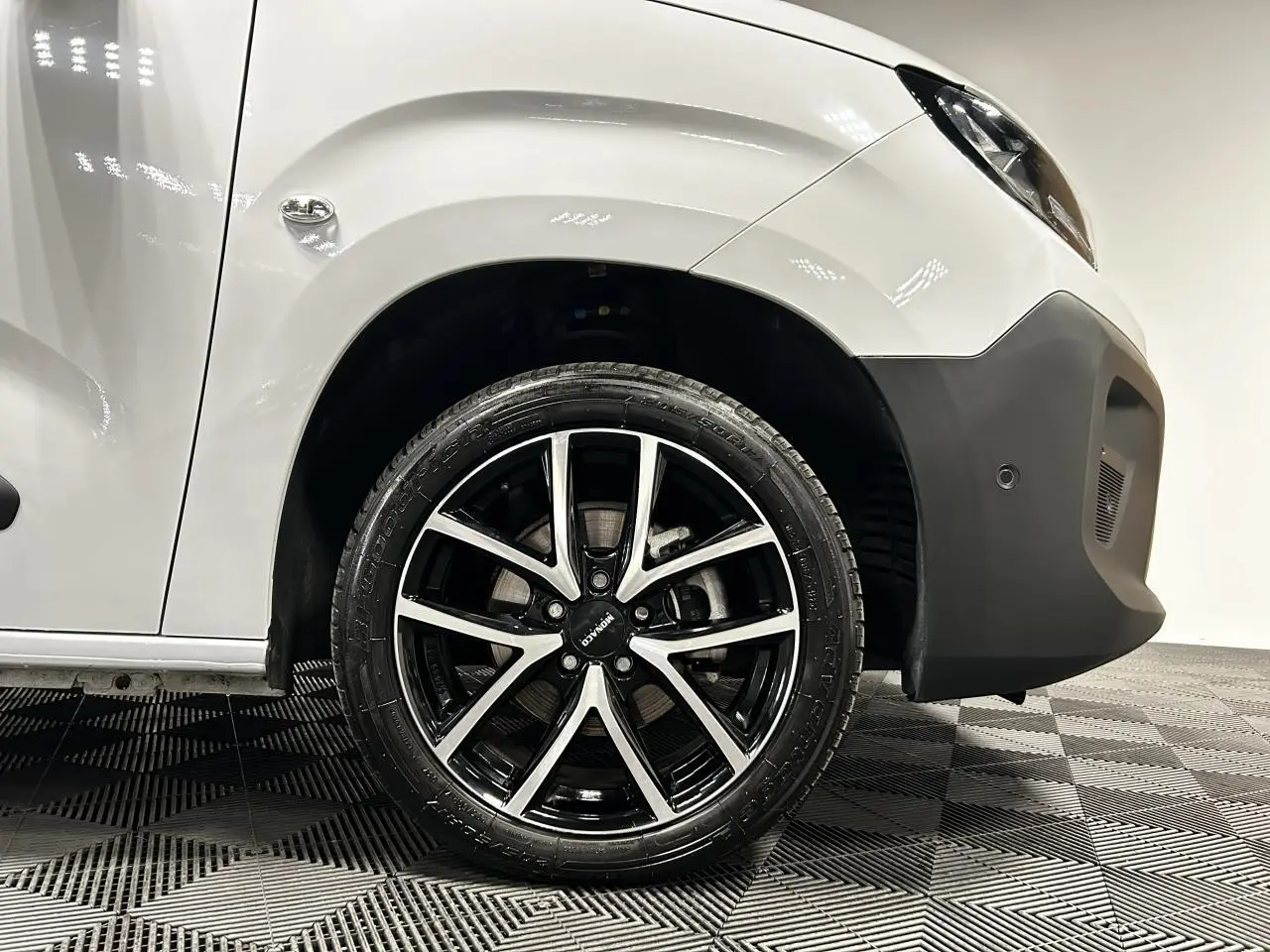 Gros plan sur la roue avant droite avec jante alu 17 pouces du Peugeot Partner blanc Banquise, partie avant visible.