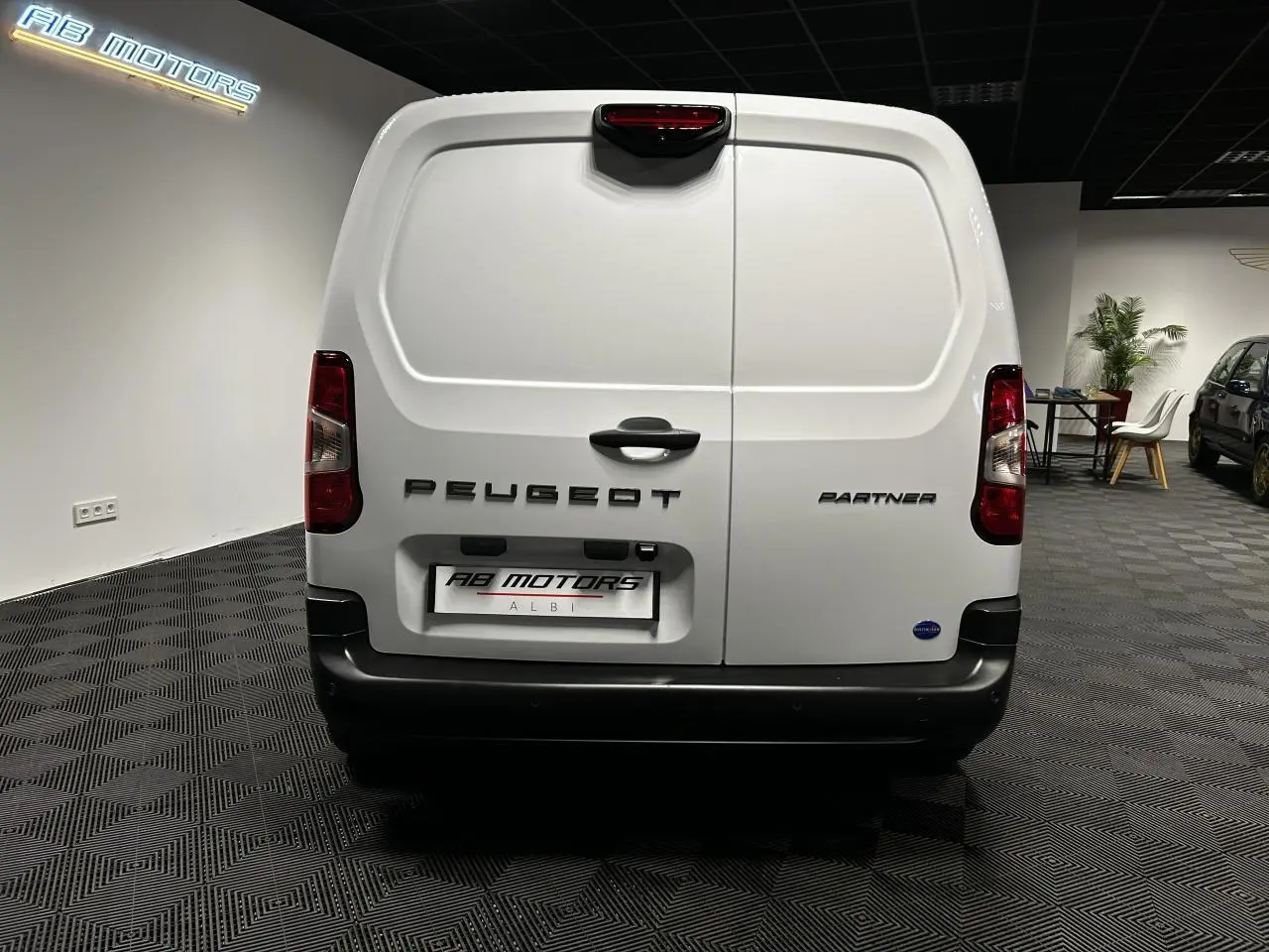 Vue arrière du Peugeot Partner blanc banquise 2025 avec portes battantes et pare-chocs noir dans un showroom.