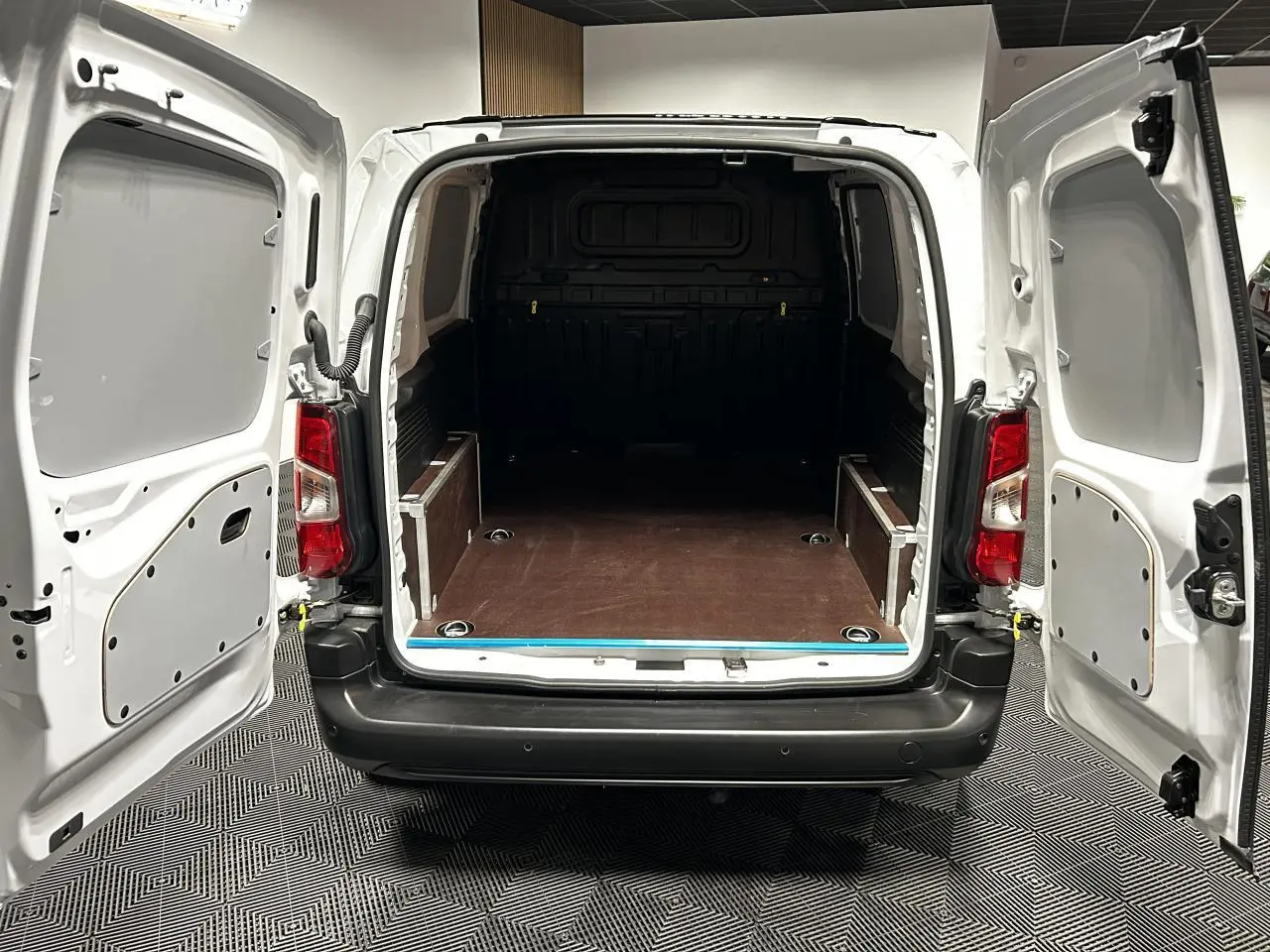 Vue arrière du Peugeot Partner blanc banquise 2025 avec portes battantes ouvertes et plancher de chargement en bois.
