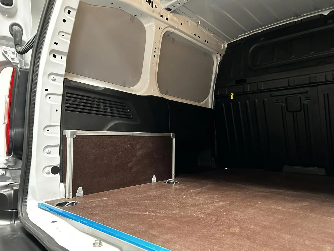 Vue intérieure arrière du Peugeot Partner blanc Banquise, plancher bois antidérapant avec anneaux d’arrimage visibles.