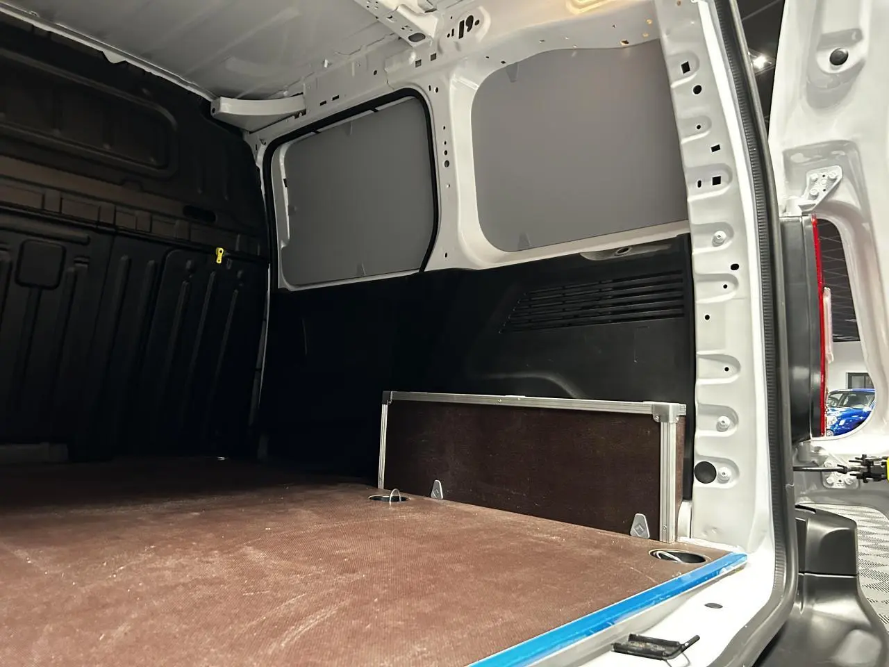 Vue intérieure arrière du Peugeot Partner blanc Banquise, montrant la zone de chargement avec plancher bois antidérapant et anneaux d’arrimage.