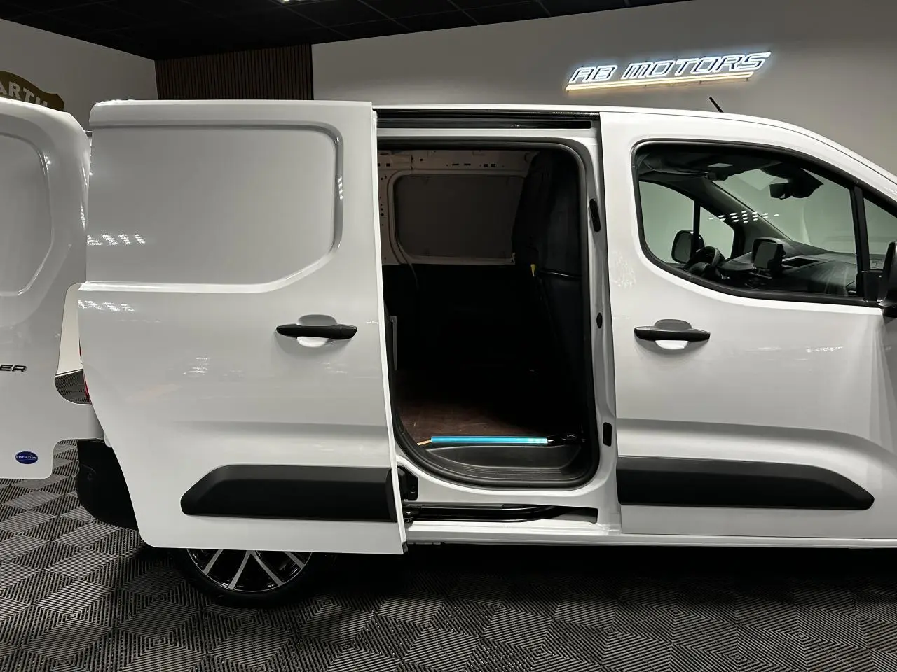 Vue latérale droite d’un Peugeot Partner blanc Banquise avec porte coulissante ouverte montrant l’espace de chargement.