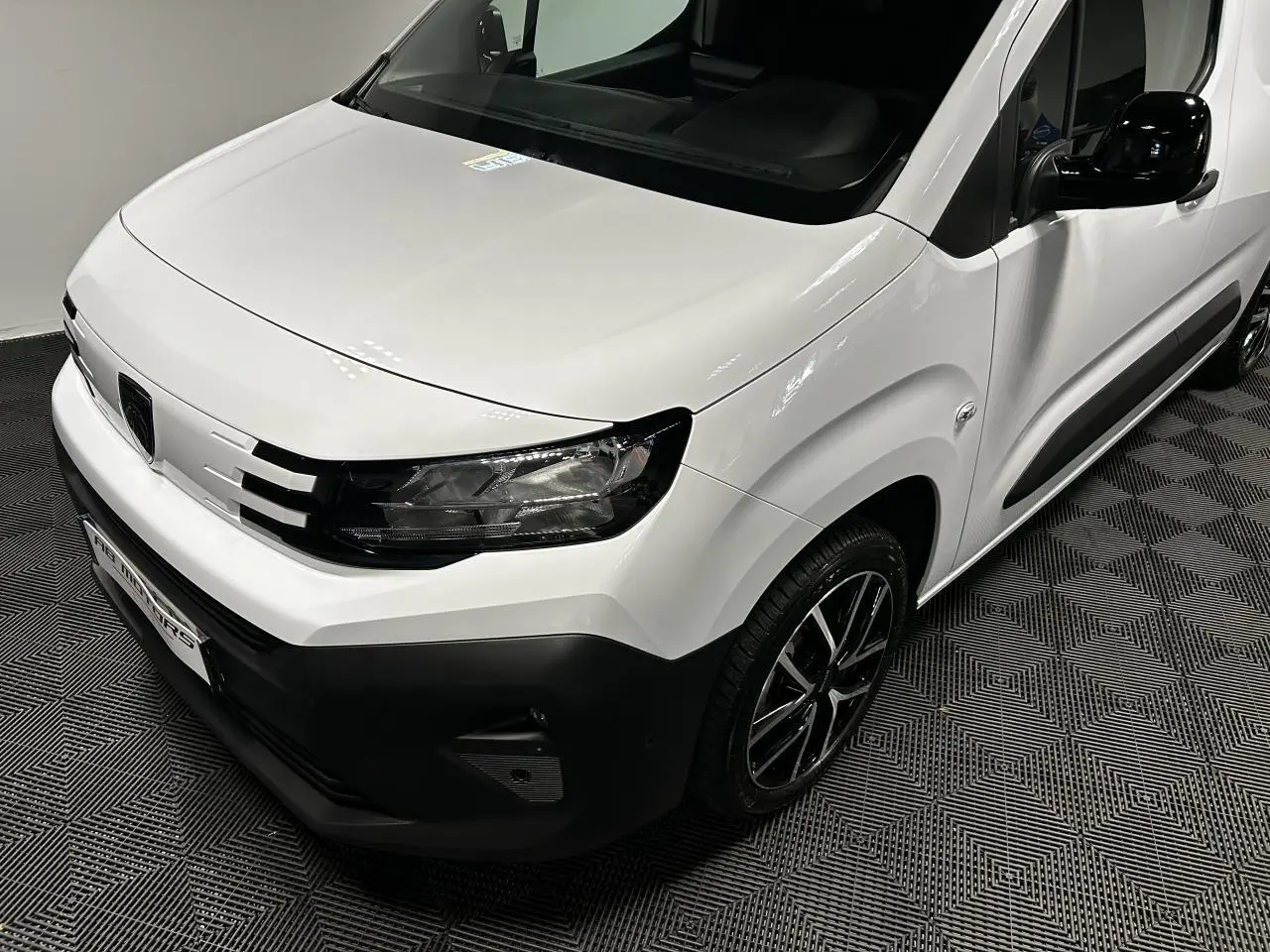 Vue 3/4 avant droit du Peugeot Partner blanc Banquise avec jantes alliage 17 pouces et rétroviseur noir brillant.