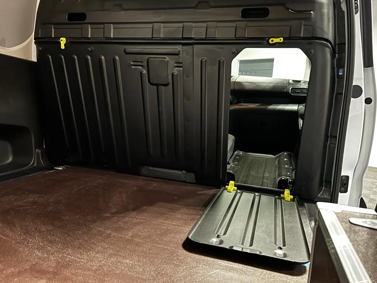 Vue intérieure du coffre du Peugeot Partner blanc banquise 2025, avec cloison noire et plancher bois antidérapant.