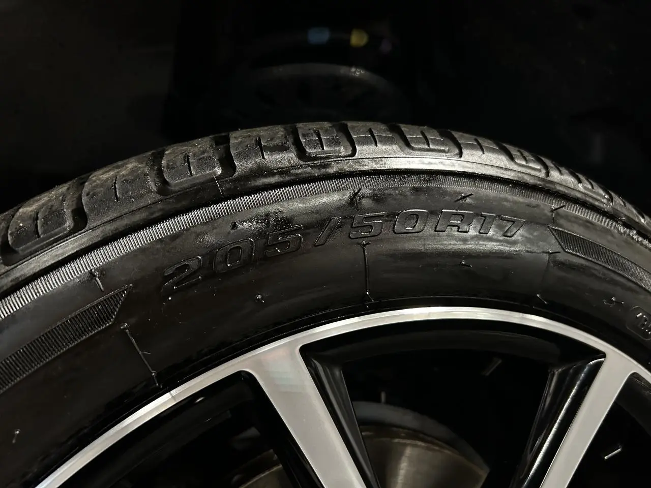 Gros plan sur la jante alu 17 pouces et le pneu 205/50R17 du Peugeot Partner blanc banquise, éclairage sombre.