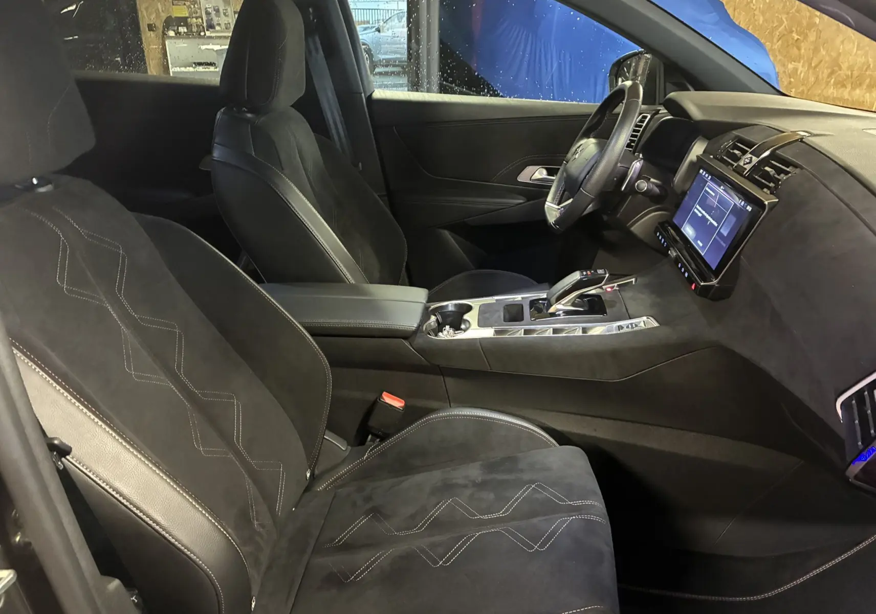 Vue intérieure côté conducteur du DS7 E-TENSE 2024, sièges noirs en alcantara avec surpiqûres et console centrale moderne.