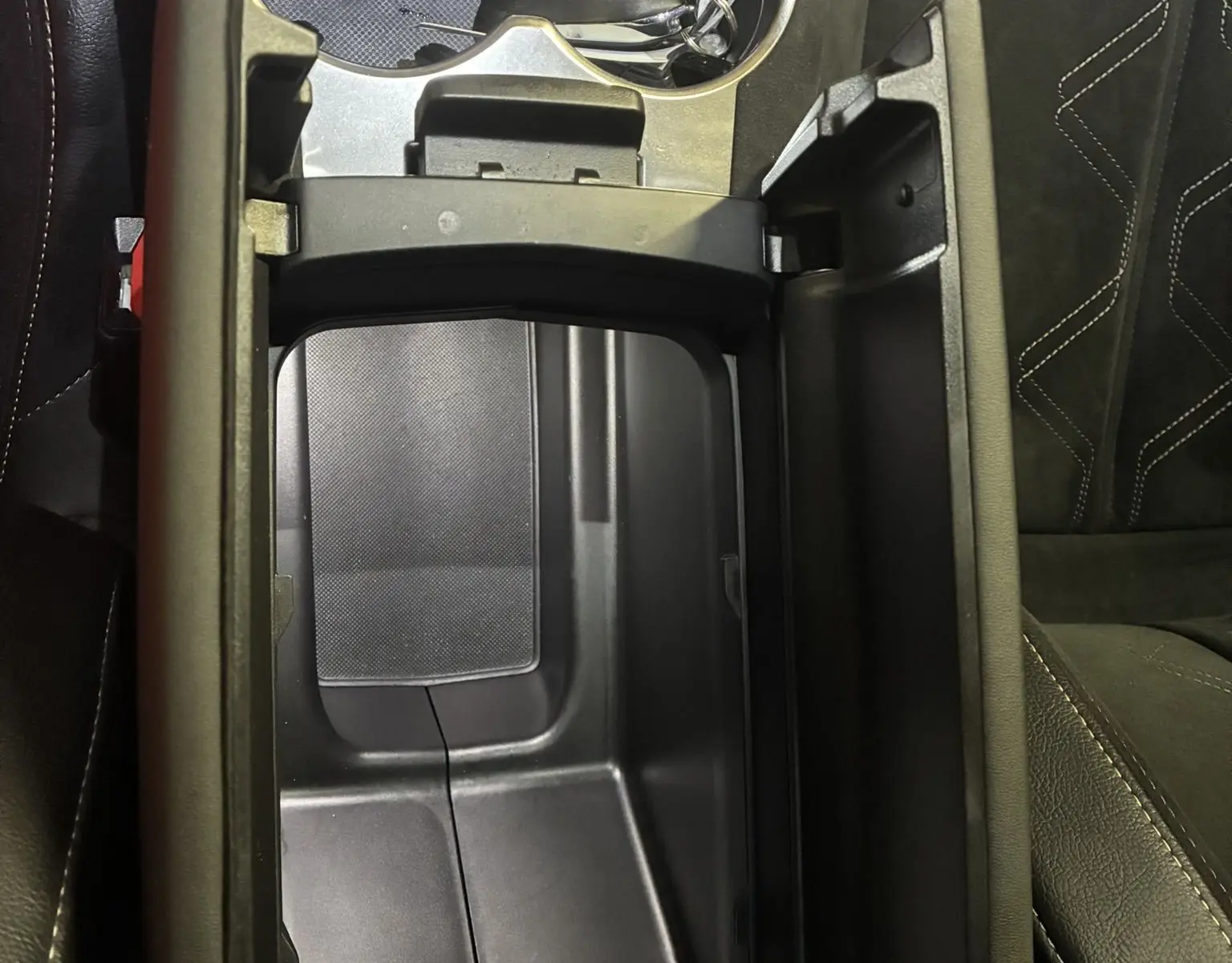 Vue plongeante sur la console centrale noire ouverte du DS7 E-TENSE 2024 avec porte-gobelets et clé posée.