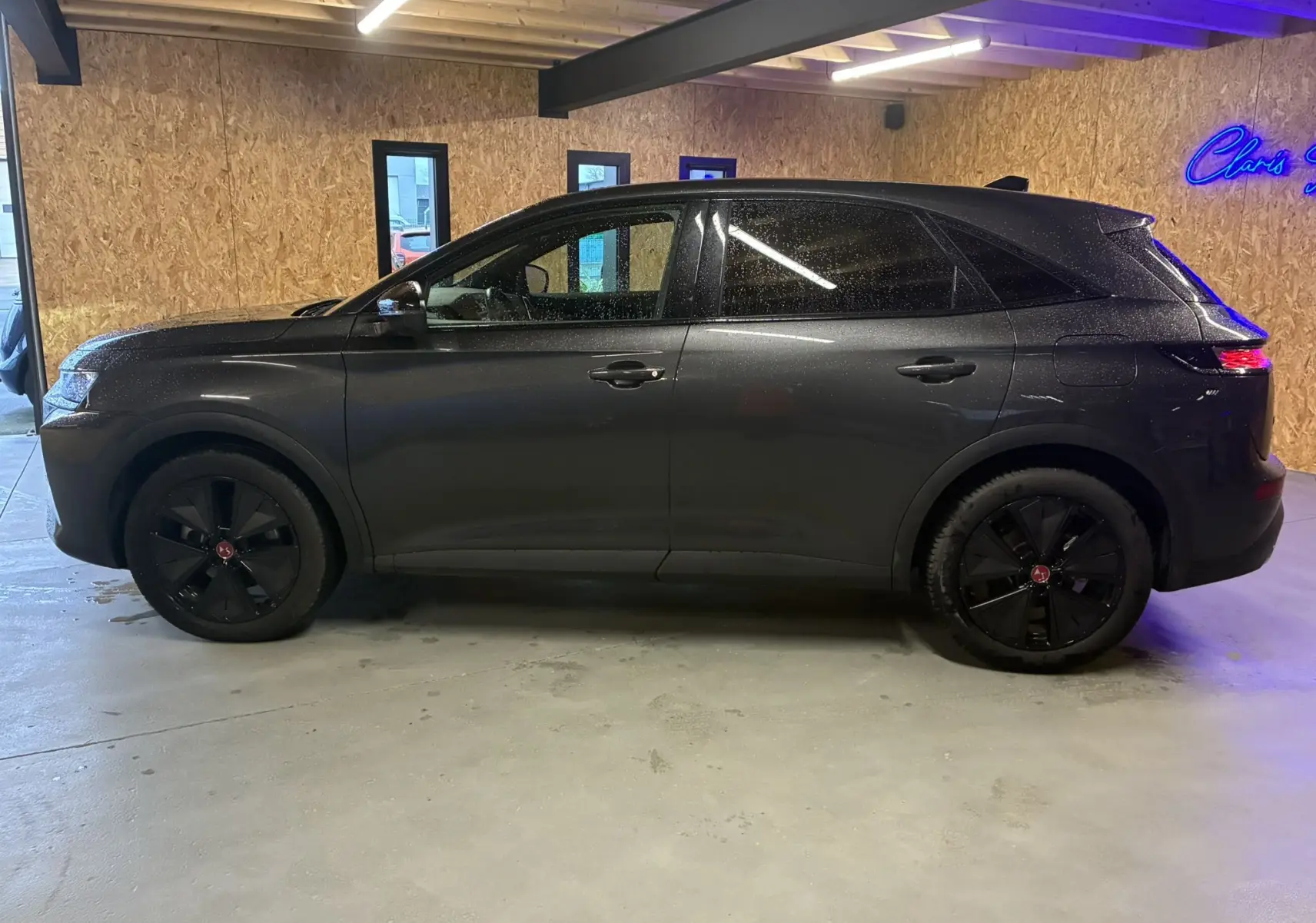 Vue de profil côté gauche d’un DS7 E-TENSE gris 2024 avec jantes noires et toit légèrement incliné, garé en intérieur.