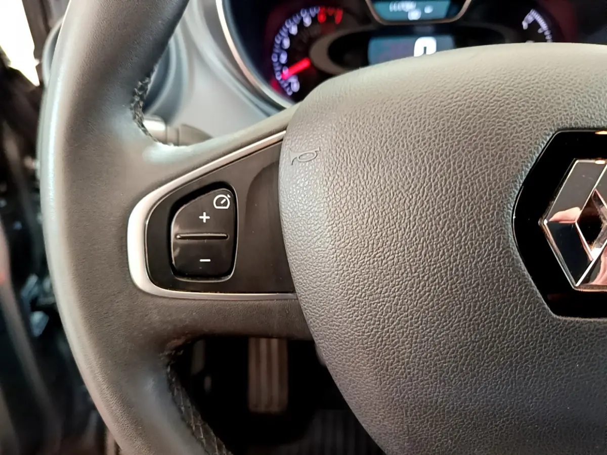 Gros plan sur le volant cuir noir de la Renault Captur gris foncé, avec commandes multifonctions visibles à gauche.