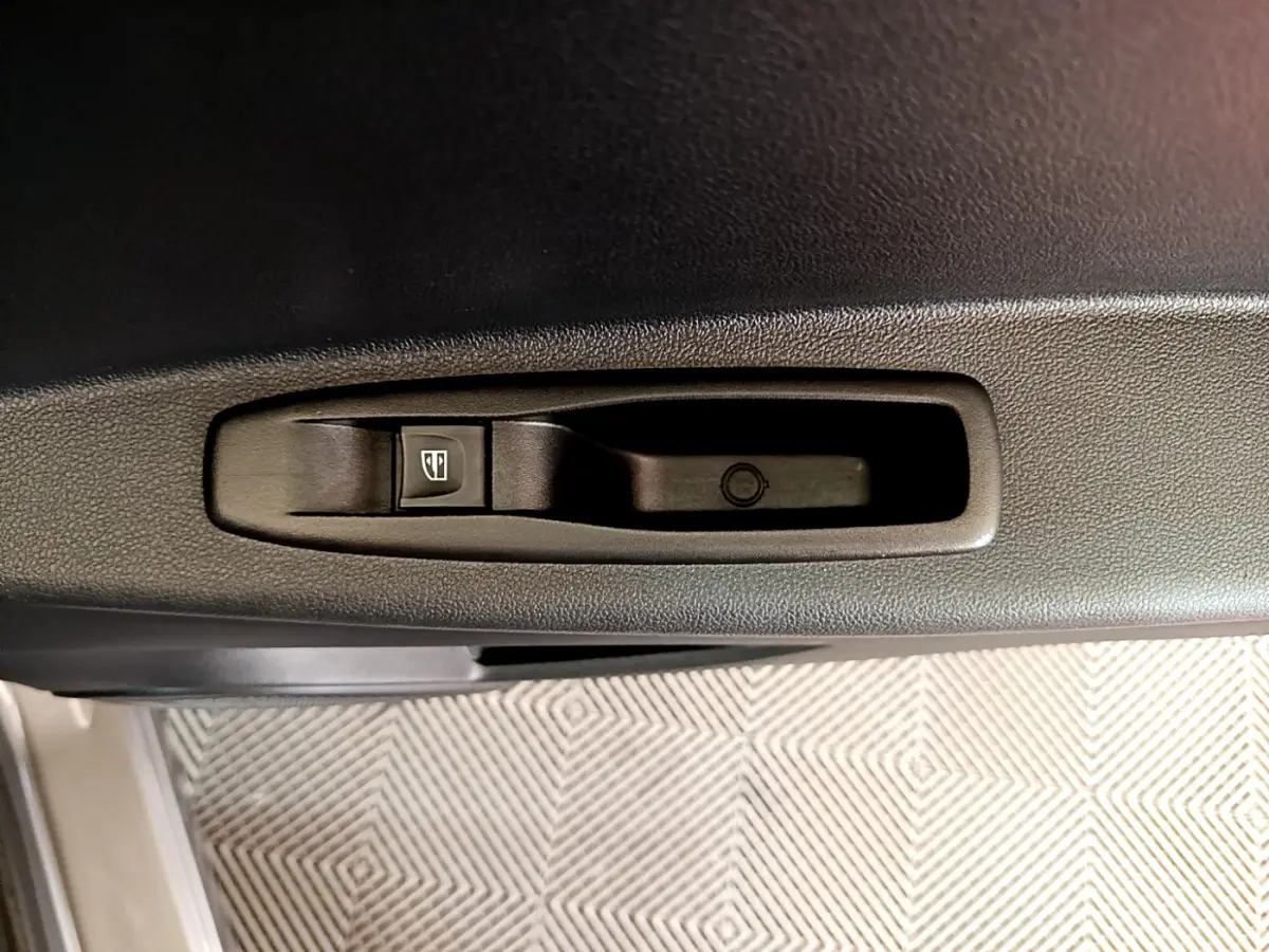 Gros plan sur le bouton de commande de la vitre électrique dans la portière intérieure d’un Renault Captur gris foncé.