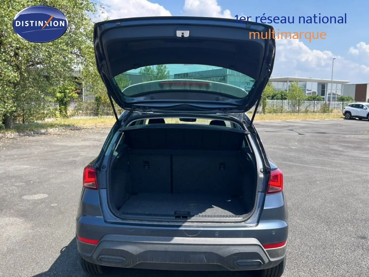 Vue arrière d'un SEAT Arona gris Magnetic Metal avec coffre ouvert, toit blanc visible en extérieur sous ciel bleu.