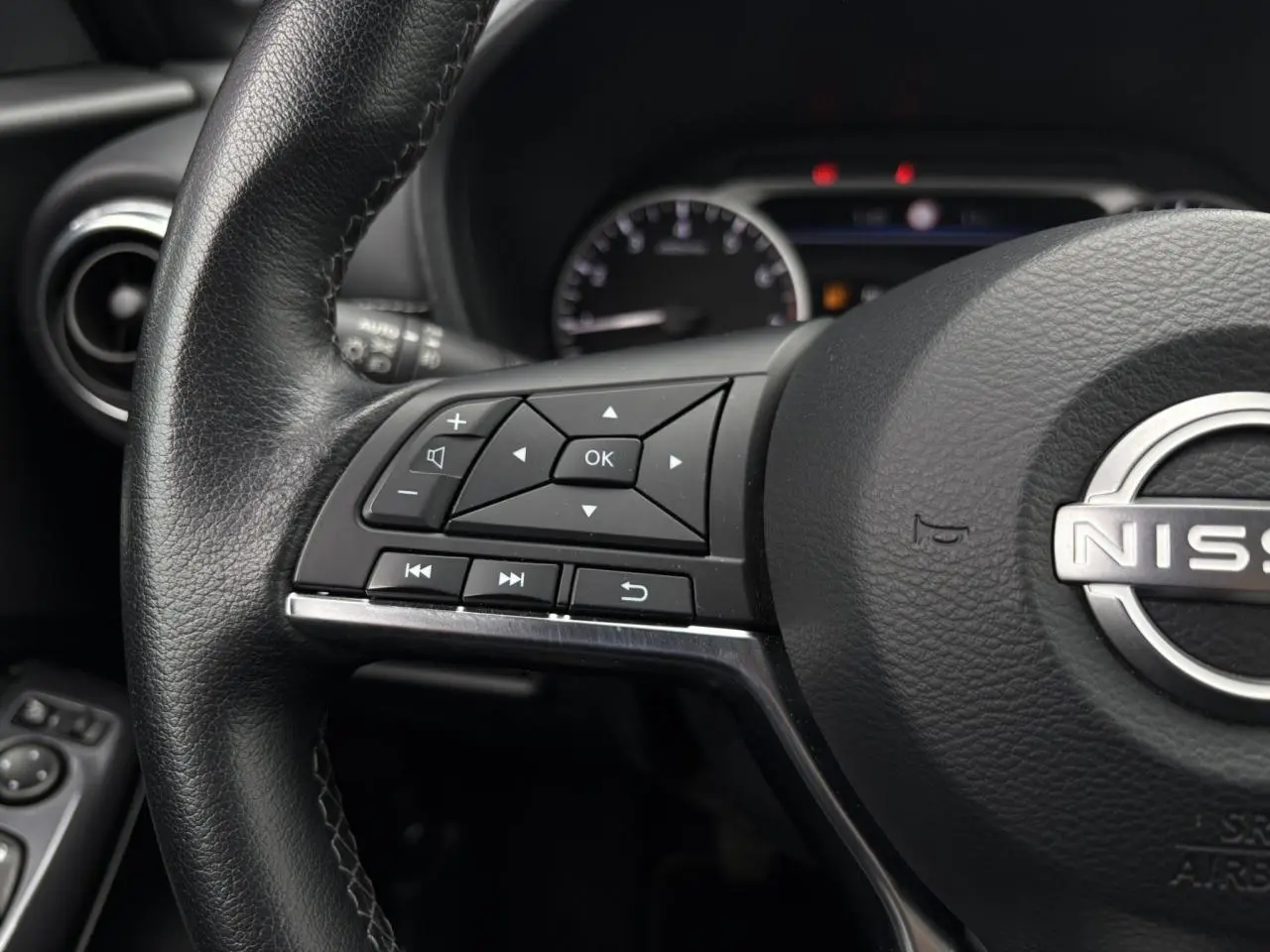 Gros plan sur le volant noir du Nissan Juke 2024, avec commandes multifonctions et logo Nissan au centre.