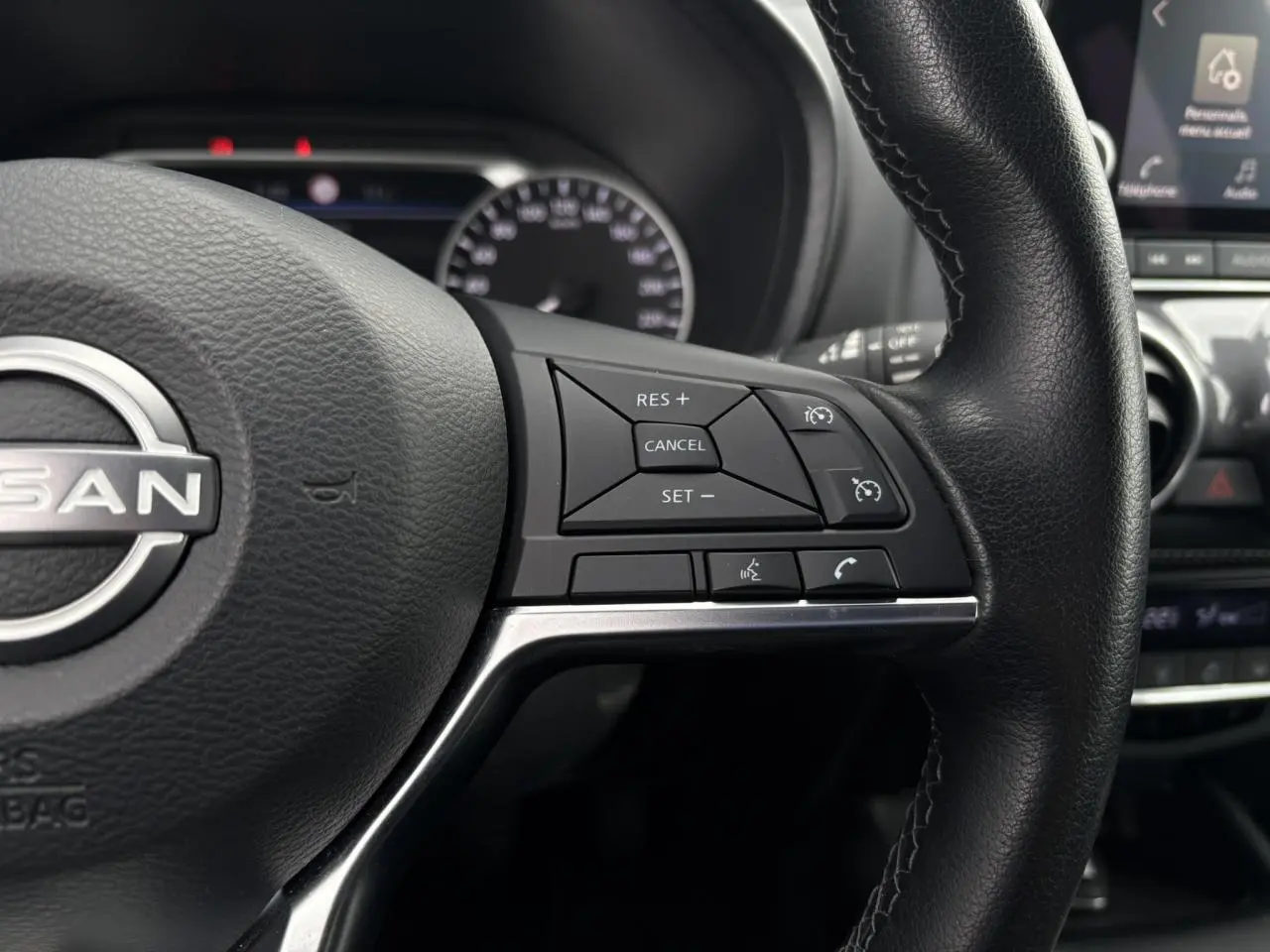 Gros plan sur le volant noir du Nissan Juke 2024 avec commandes de régulateur de vitesse et téléphone intégrées.