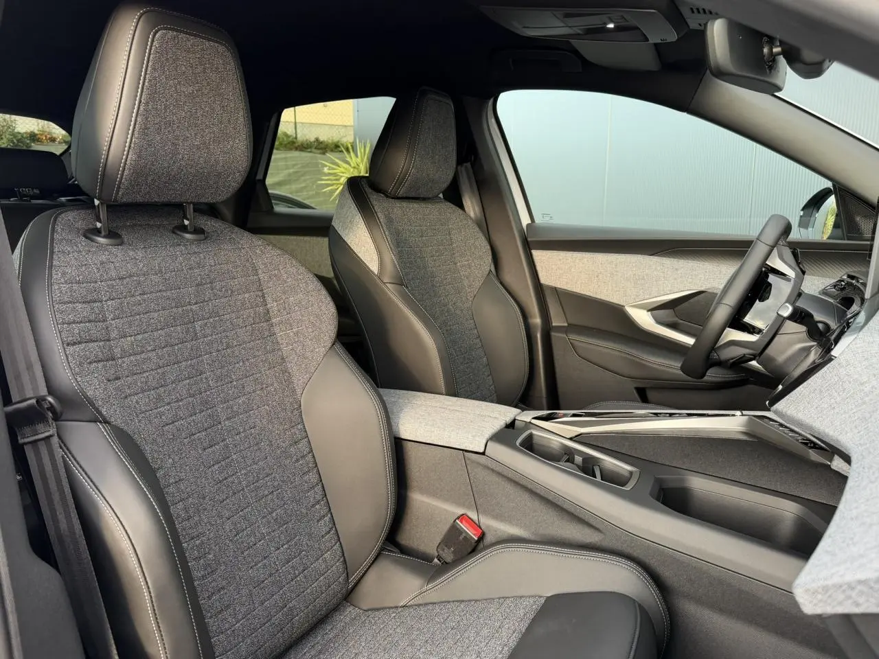 Vue intérieure côté droit du Peugeot 3008 Hybrid 145 Allure 2025, sièges tissu gris et cuir noir avec console centrale moderne.