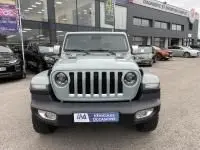 Vue avant d'une Jeep Wrangler Unlimited 2023 vert métal, hybride rechargeable, garée devant un concessionnaire.