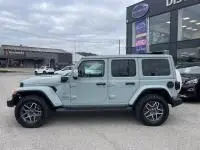 Vue de profil droit d'un Jeep Wrangler Unlimited vert métal 2023 hybride rechargeable devant un concessionnaire.