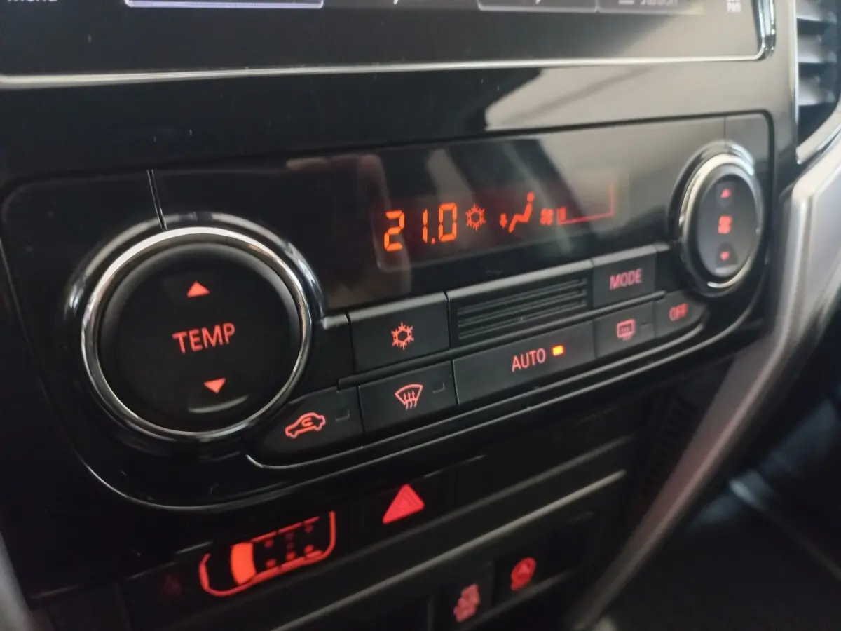 Gros plan sur la commande de climatisation digitale du Mitsubishi L200 gris foncé, affichant 21°C en mode automatique.